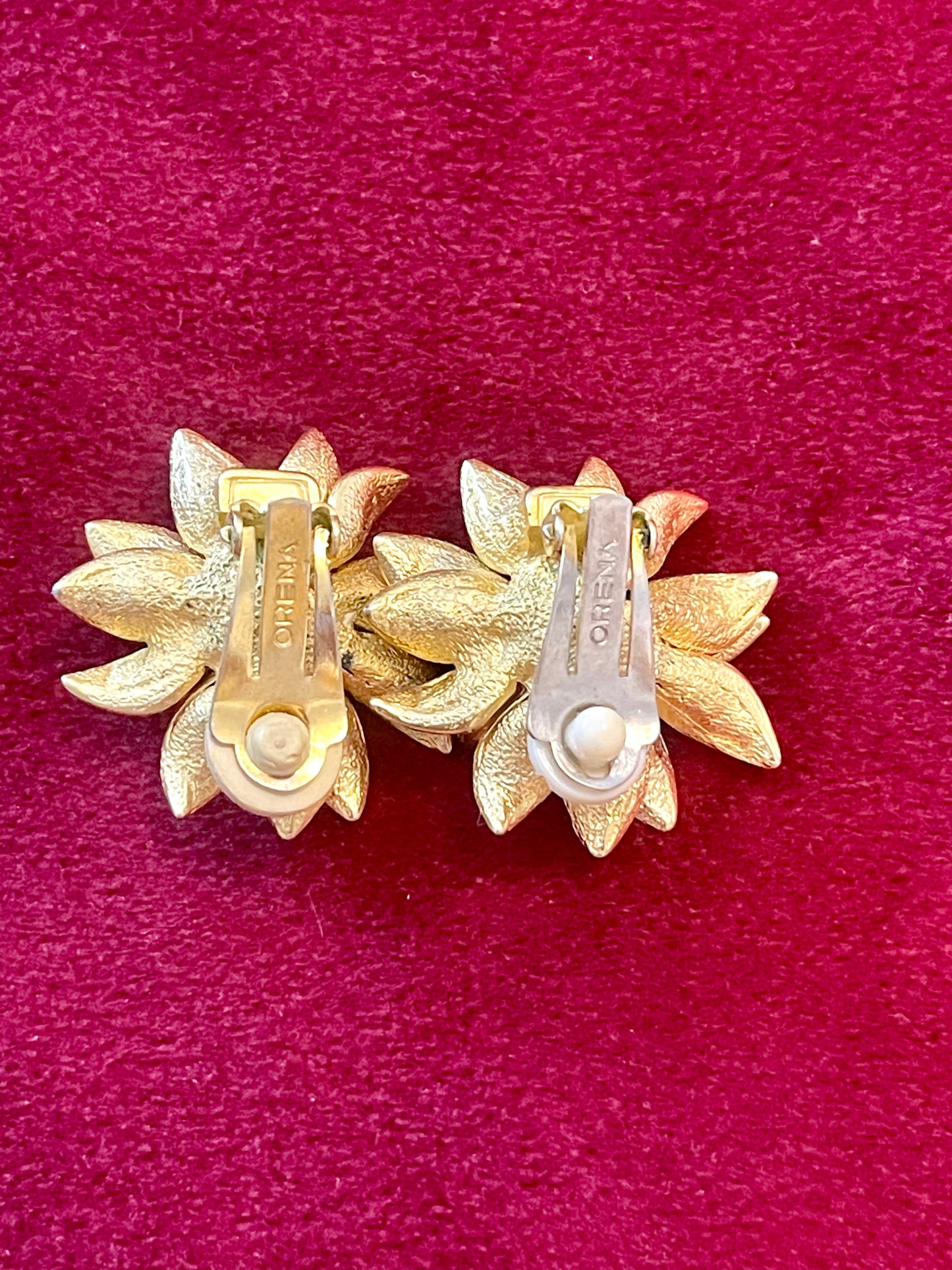 Close up in hallmark signature Orena Paris vintage gold sunflower-shaped earrings on a red background Showing signs of wear 