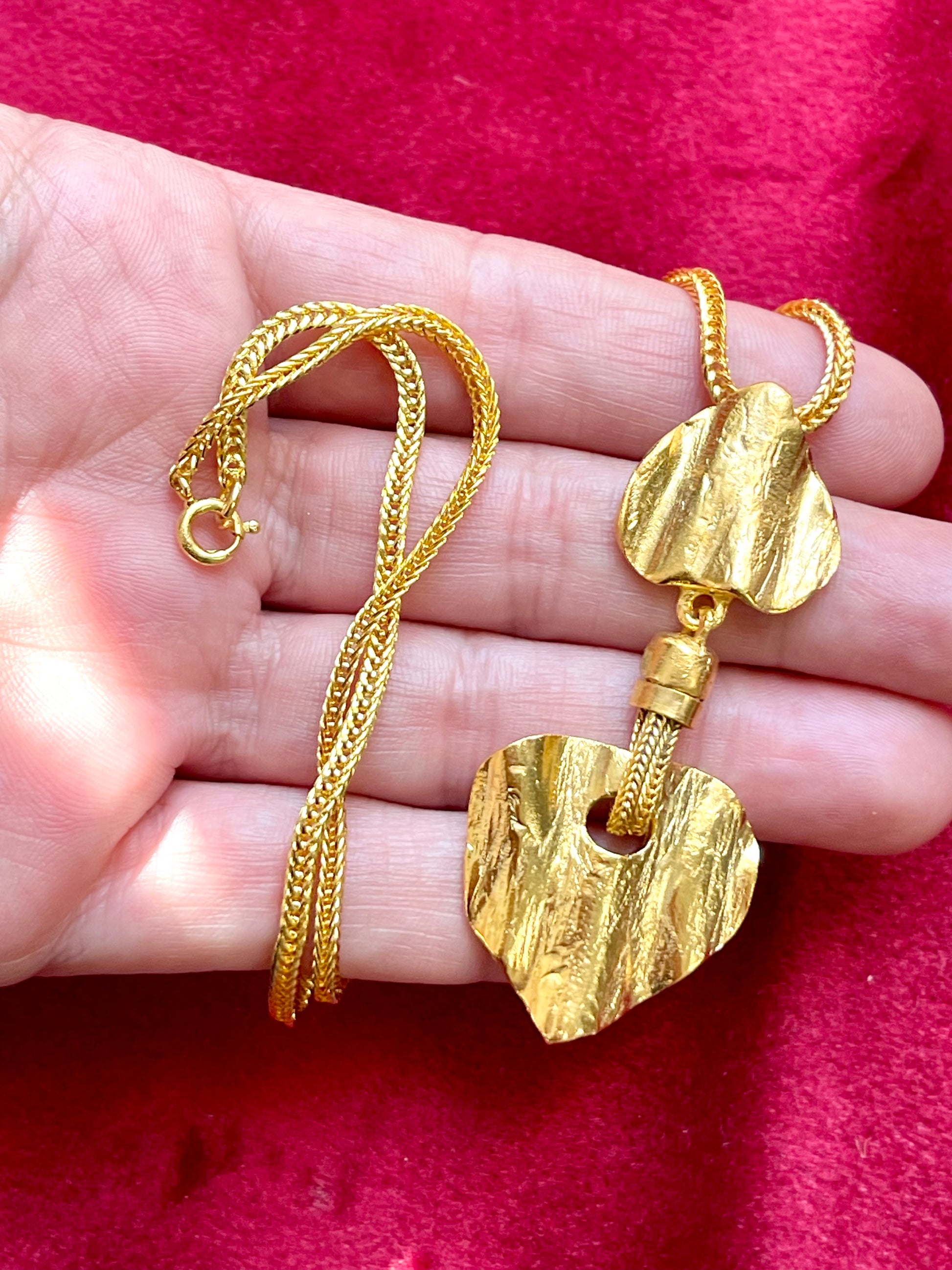 Gold-tone repurposed Yves Saint Laurent necklace displayed on hand. The pendant features two textured, sculptural heart-shaped elements in a brushed gold finish, 