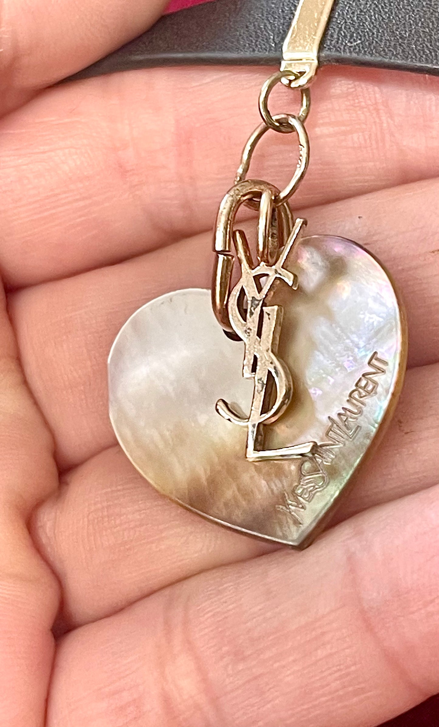 Heart-shaped YSL pendant on a hand showing details of signs of wear Yves Saint Laurent vintage leather bracelet 