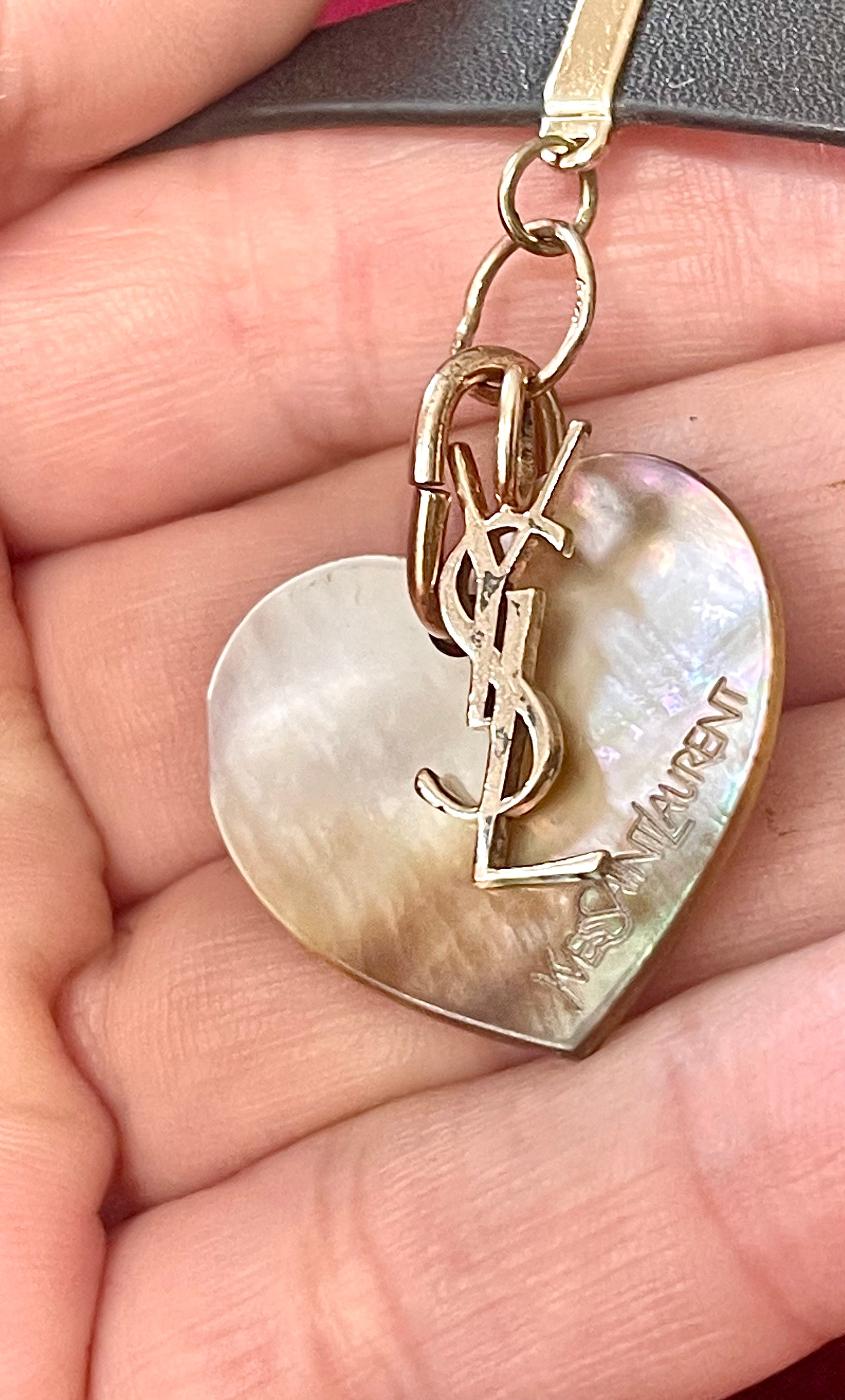 Heart-shaped YSL pendant on a hand showing details of signs of wear Yves Saint Laurent vintage leather bracelet 
