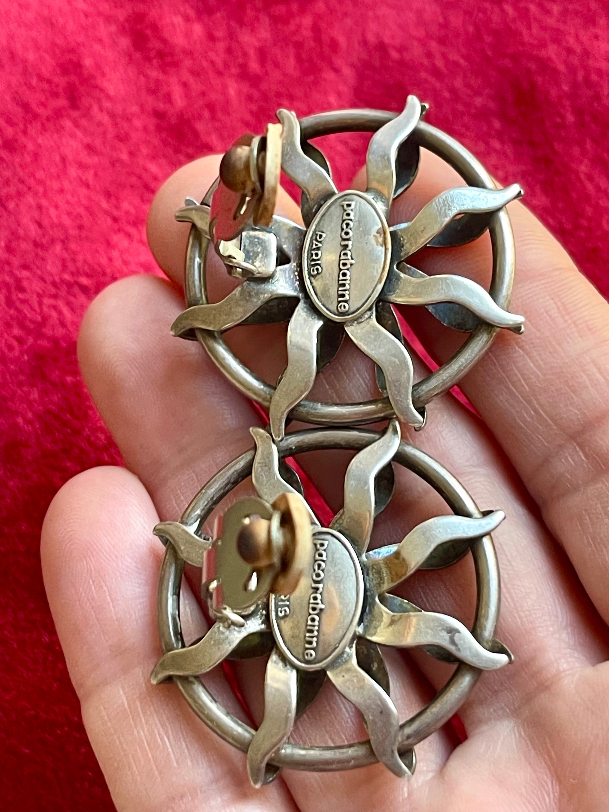 Showing back side clasp and hallmark of Vintage Paco Rabanne sun-design earrings in silver tone with black faceted stones, shown on hand 
