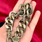 Laying flat on hand Preloved YSL bronze and grey chain worn as a statement piece against black fabric and YSL pouch 