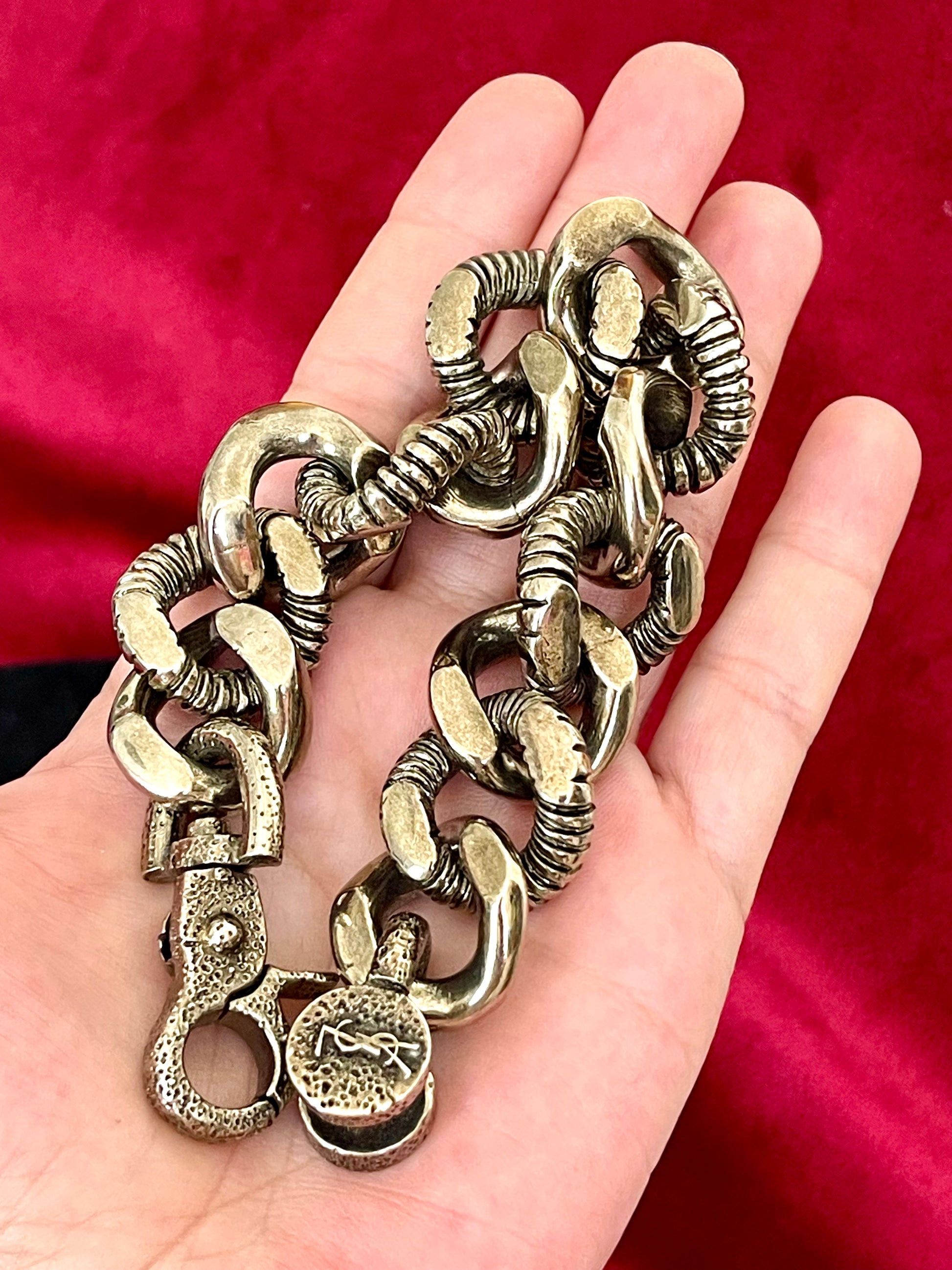 Laying flat on hand Preloved YSL bronze and grey chain worn as a statement piece against black fabric and YSL pouch 