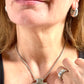 Close-up of a model wearing the vintage Yves Saint Laurent jewelry set: silver earrings with blue stones, cross pendant necklace, and matching ring