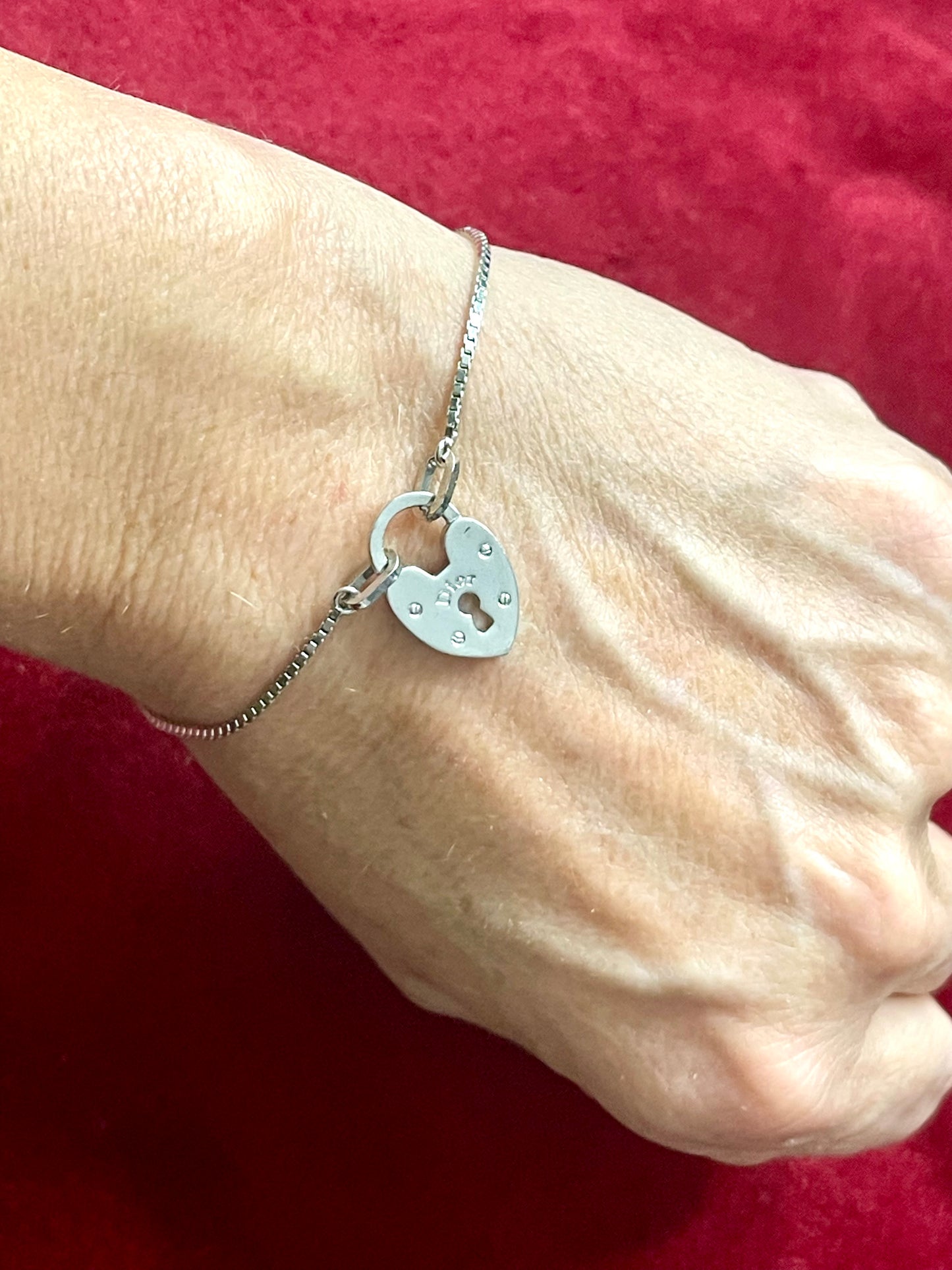Silver Dior vintage bracelet with a heart-shaped padlock charm on a wrist against a red background