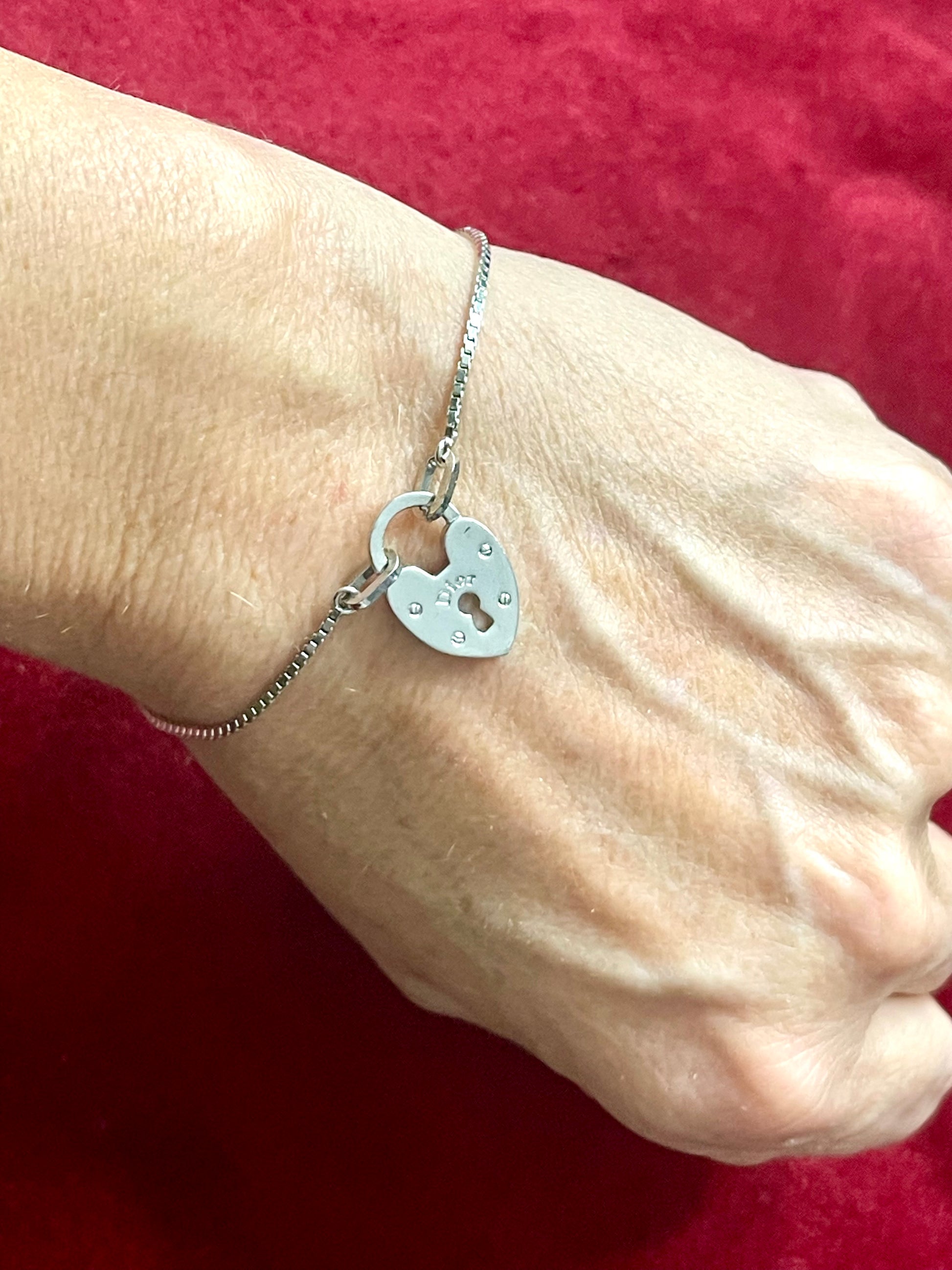 Silver Dior vintage bracelet with a heart-shaped padlock charm on a wrist against a red background