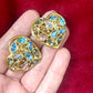 On hand Pair of 3 cm gold-tone vintage Yves Saint Laurent heart-shaped clip-on earrings decorated with multi-colored crystals, displayed on a red background