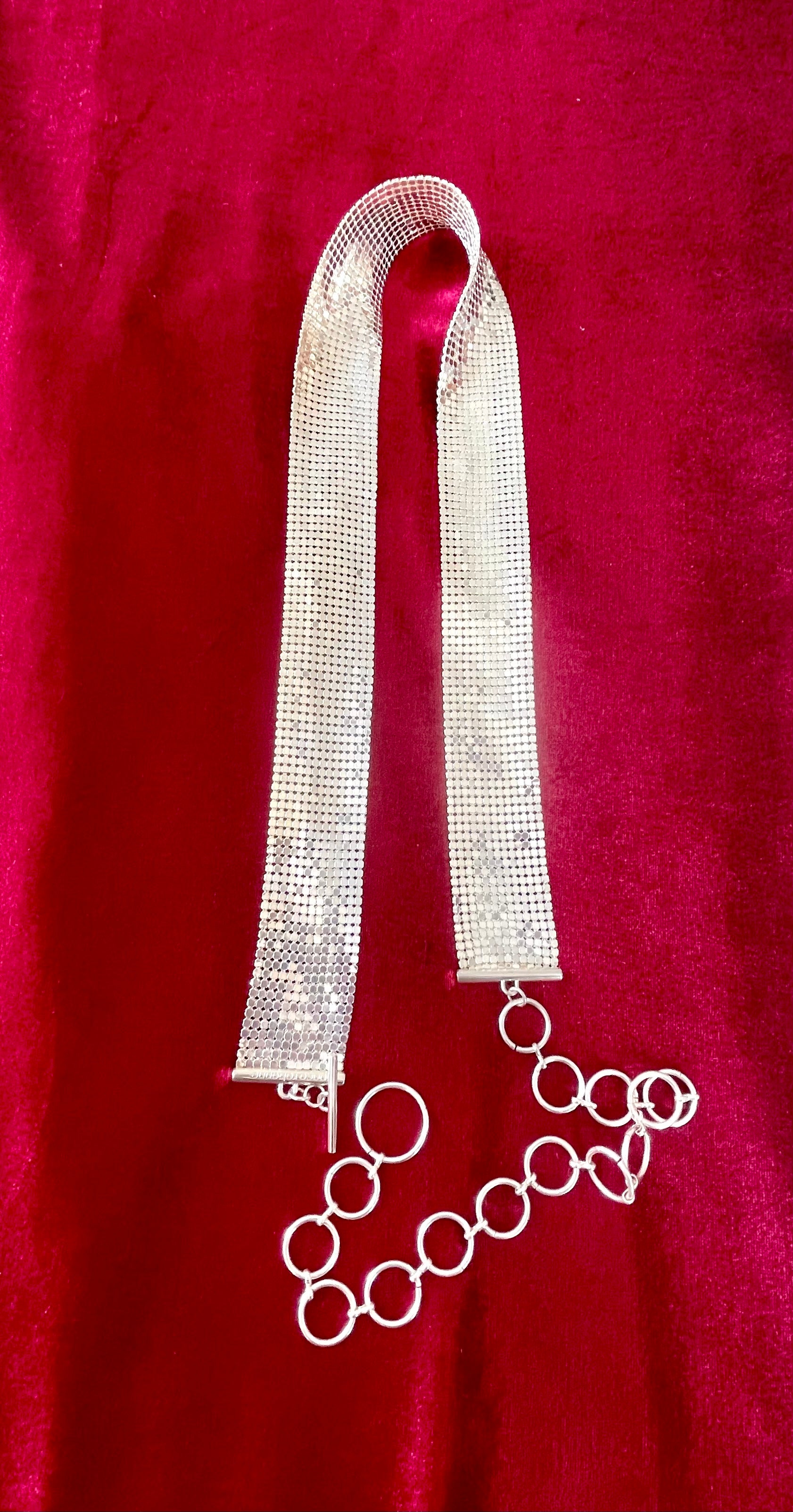 Flat lay of vintage silver Paco Rabanne mesh belt with hoops on red velvet background.