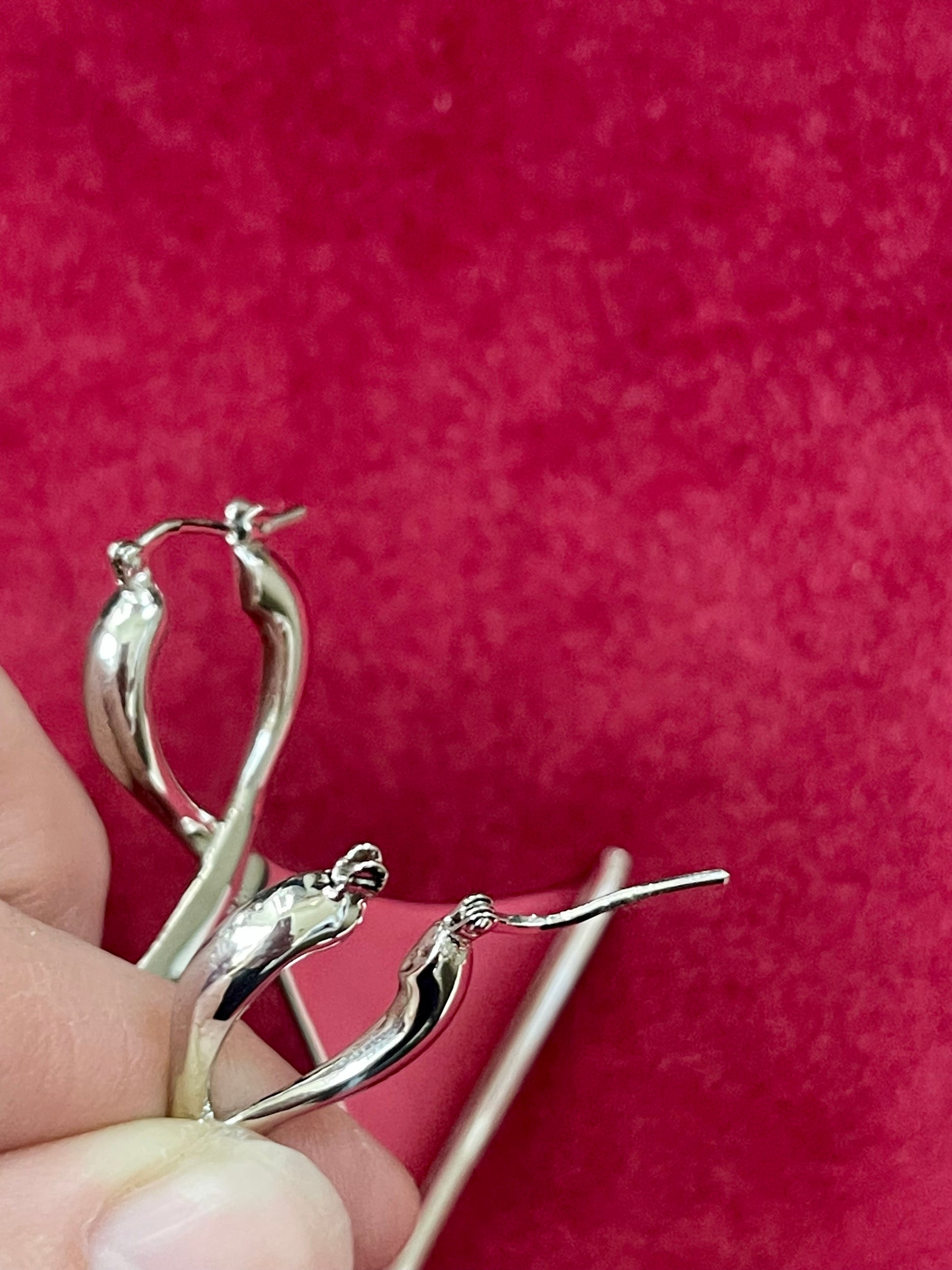 Close up on hoops of Paco Rabanne vintage rare geomtrical earrings held by a hand against a red background