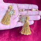 Gold tassel YSL earrings on a hand against a pink background