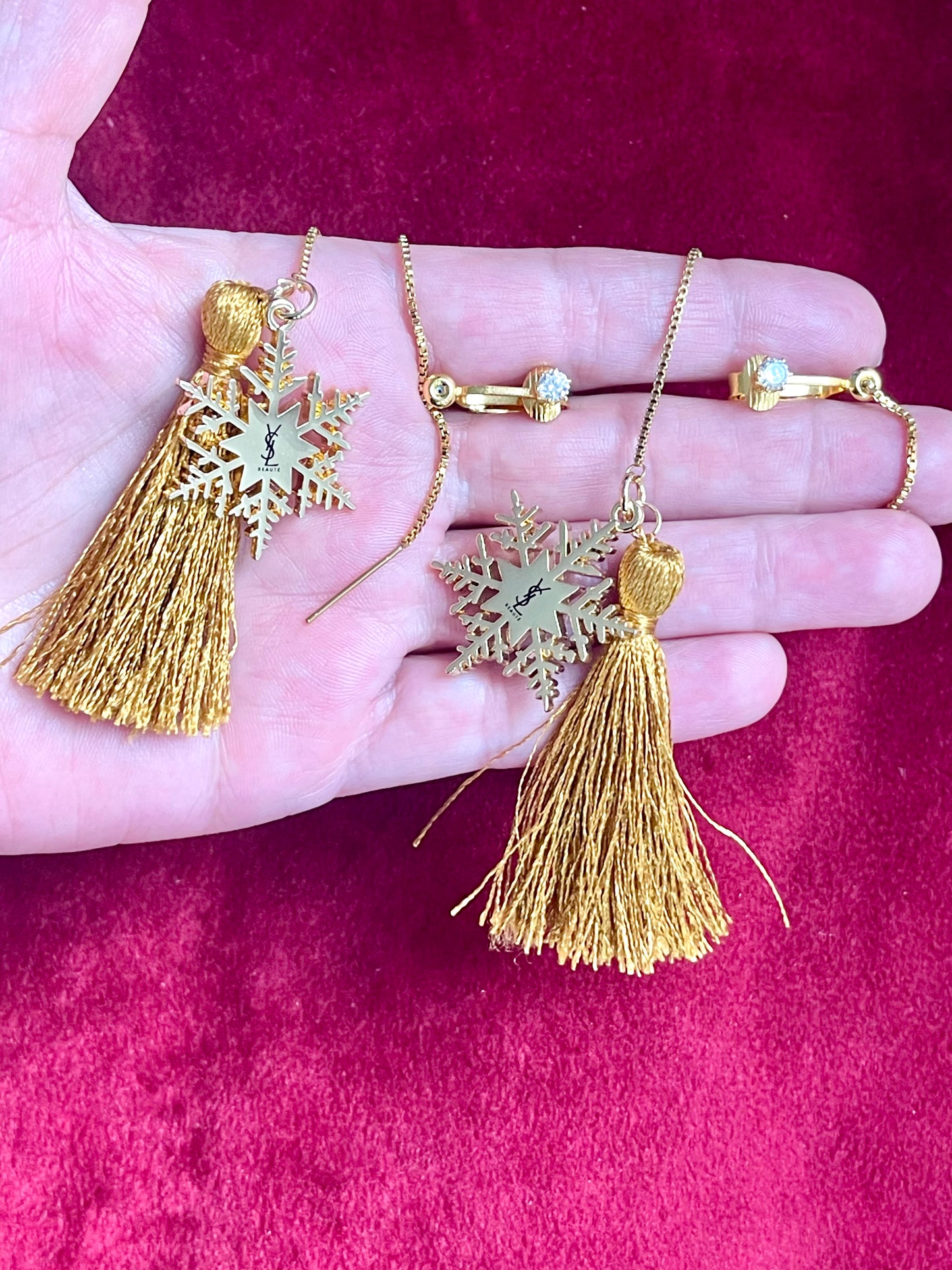Gold tassel YSL earrings on a hand against a pink background