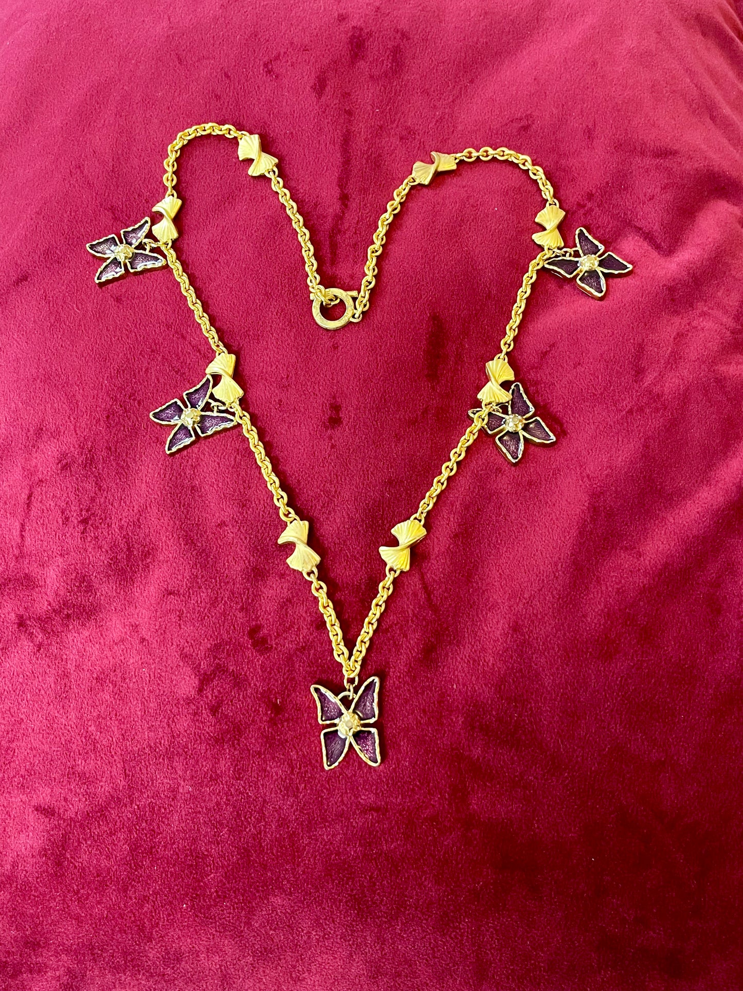 Vintage 80s five Yves Saint Laurent Butterfly Enameled pendants mounted on a Nina Ricci gold necklace, displayed on a red velvet background 