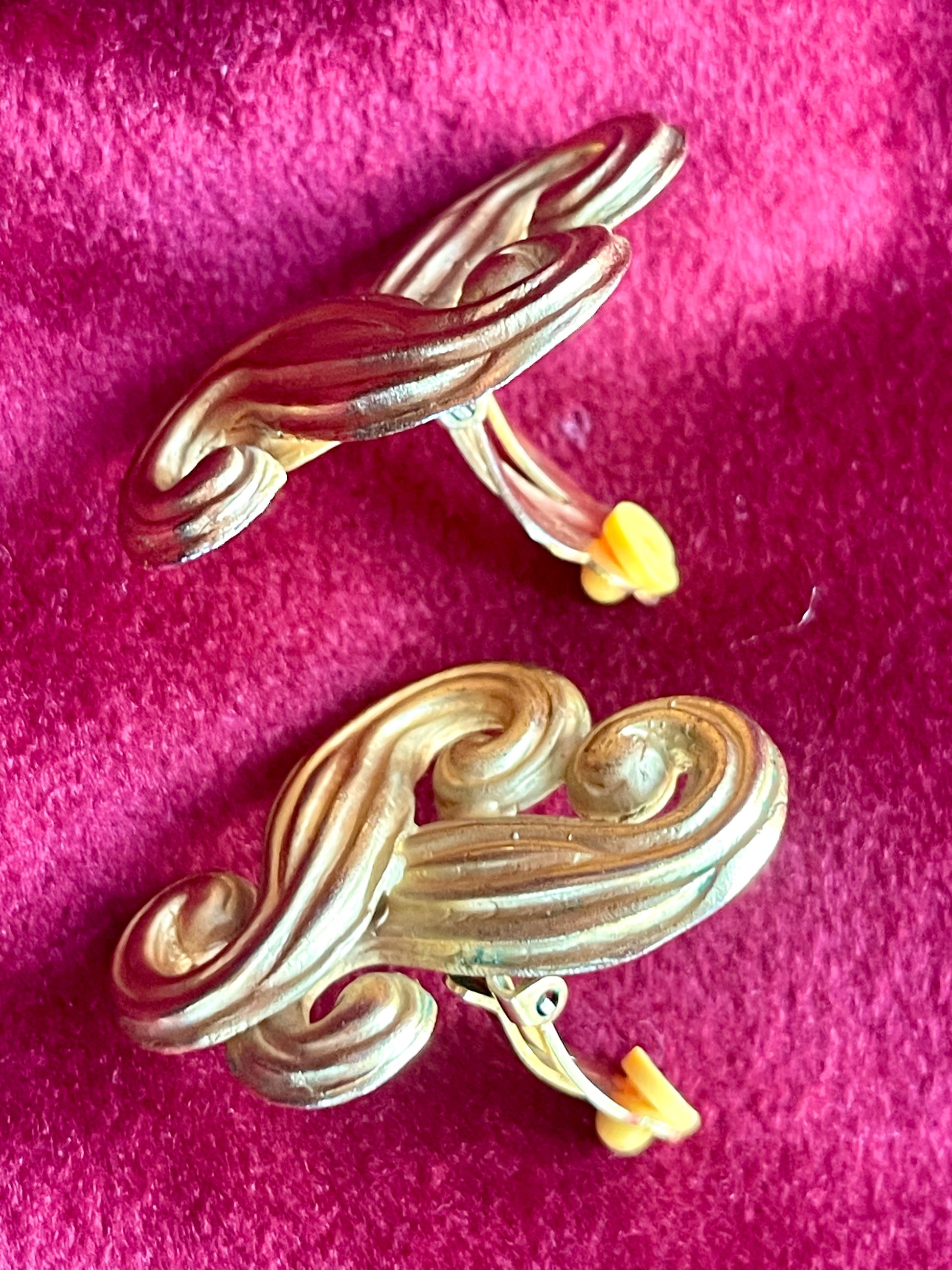 Close-up of side view vintage Nina Ricci swirly heart earrings with sculptural design in matte gold tone