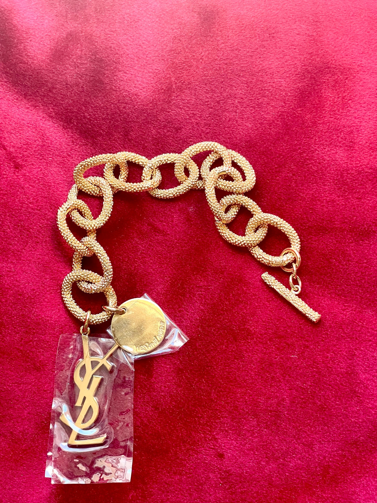 Detail view of YSL monogram charm hanging from gold vintage Yves Saint Laurent bracelet.