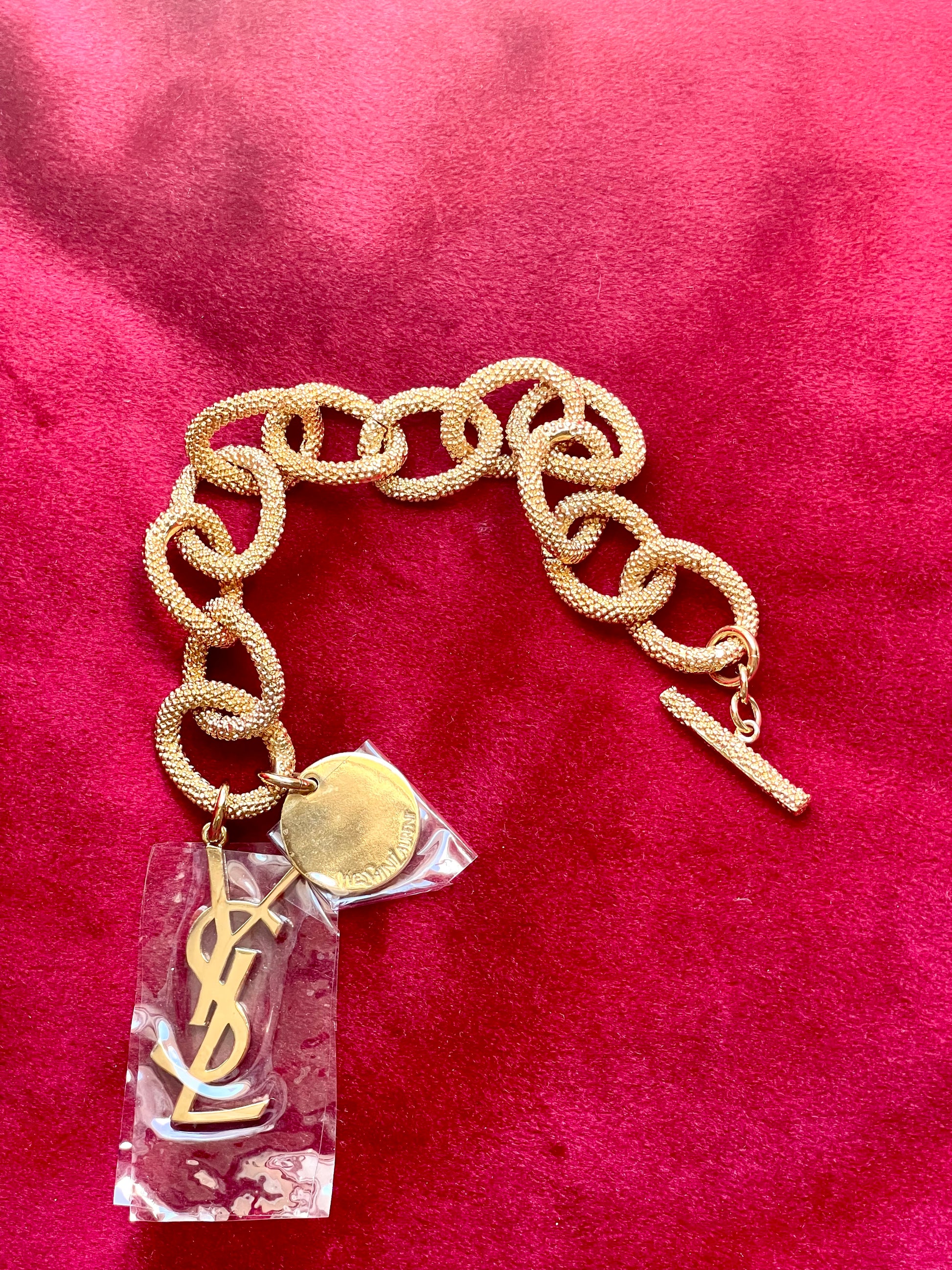 Detail view of YSL monogram charm hanging from gold vintage Yves Saint Laurent bracelet.