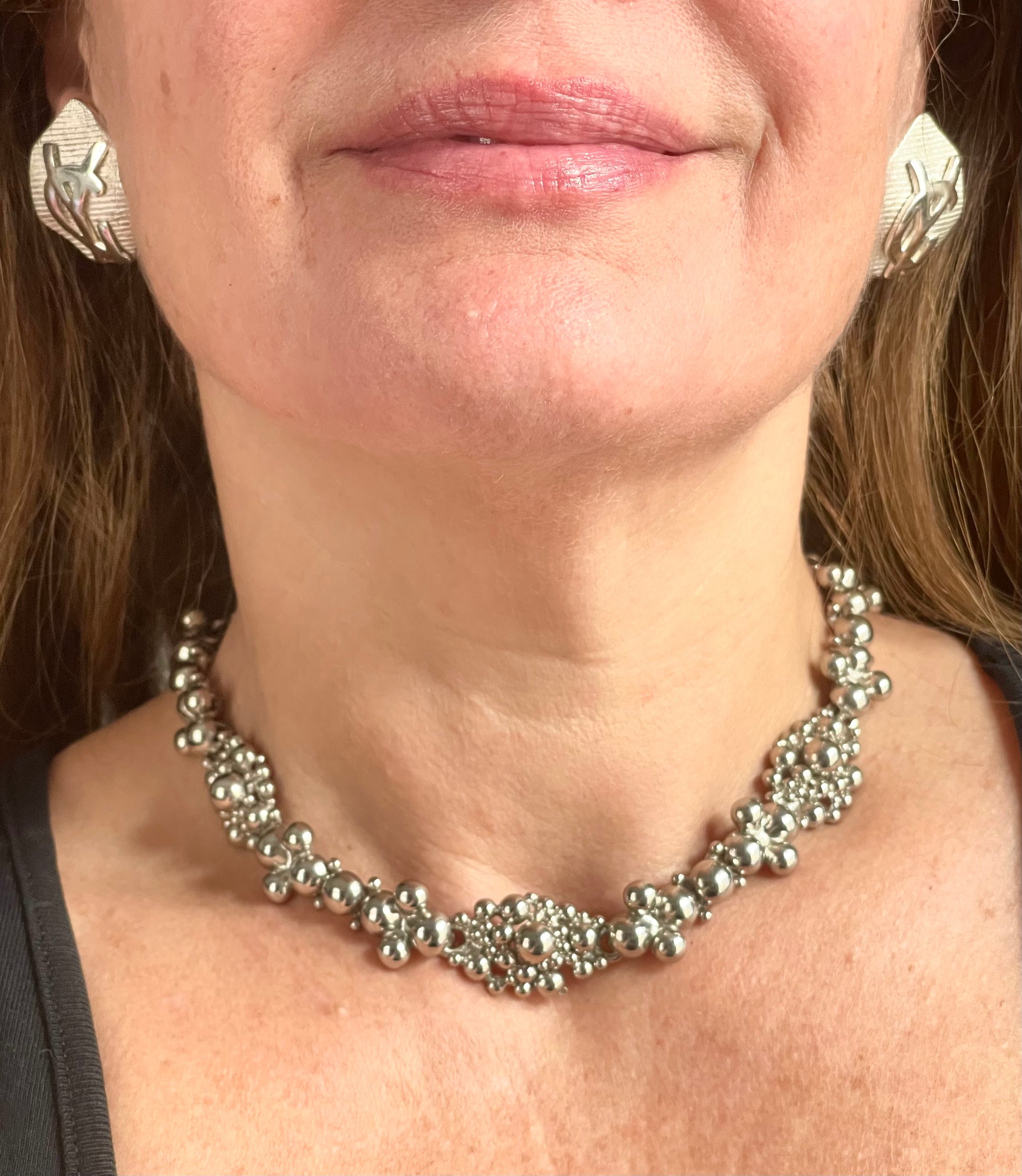 Close-up of a model wearing a vintage Yves Saint Laurent silver necklace with hexagonal YSL Monogram earrings.