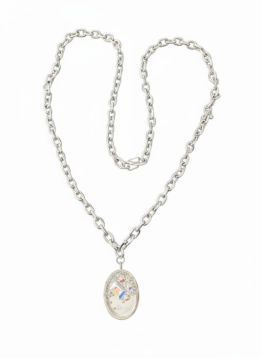 vintage Dior Cristal Boréal locket necklace displayed on a rich red velvet background. The oval pendant features iridescent crystals and ‘Dior’ engraving, attached to a silver-tone chain.