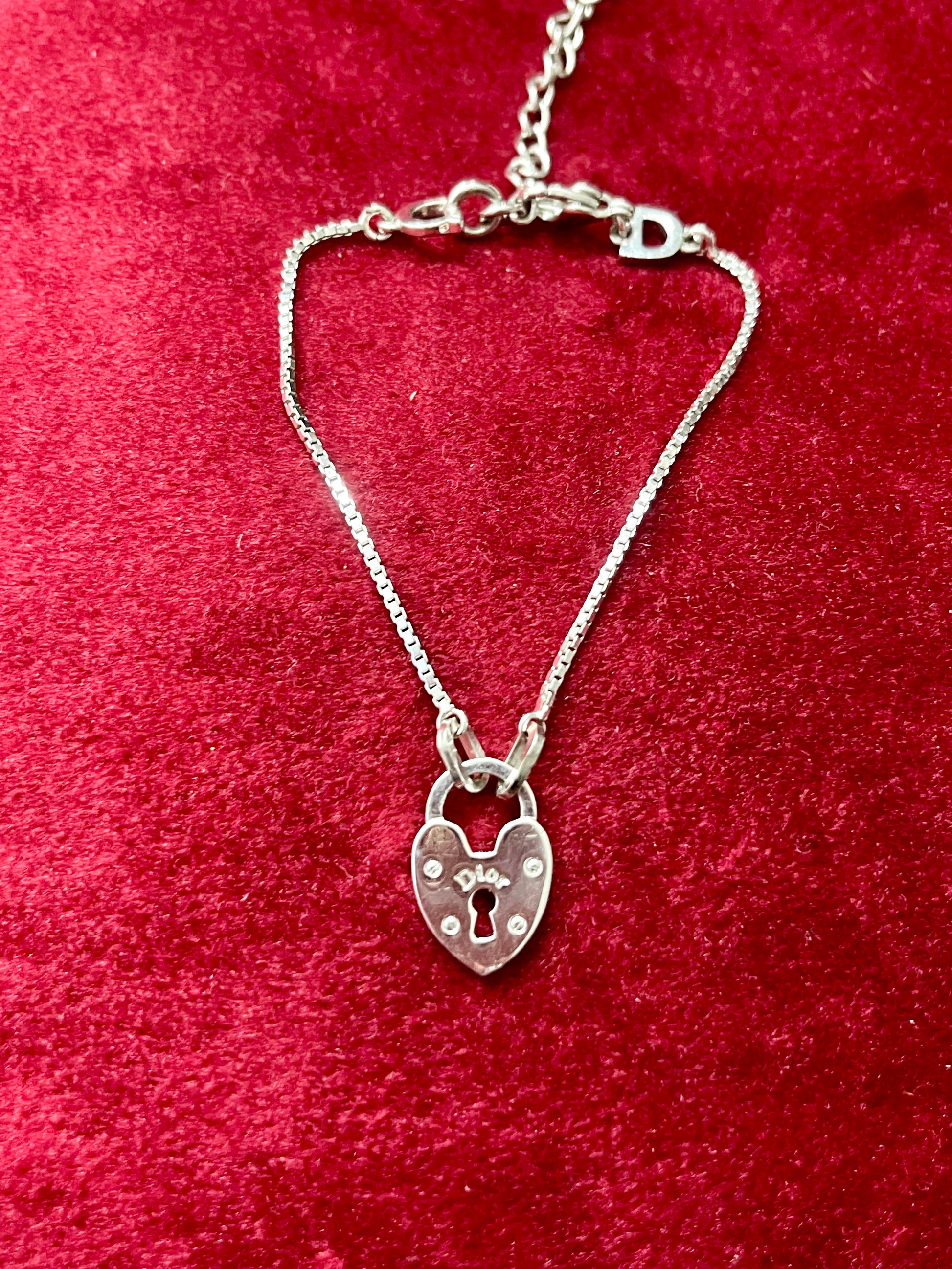 Dior silver tone bracelet with a heart -shaped lock pendant on a red textured background