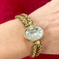 Close up Yves Saint Laurent gold bracelet with a large clear gemstone on a wrist against a red background