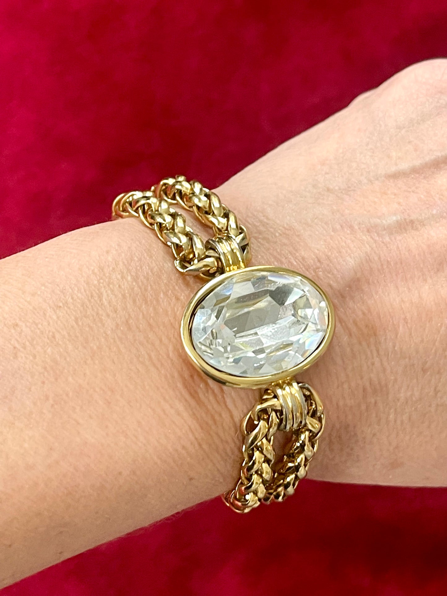Close up Yves Saint Laurent gold bracelet with a large clear gemstone on a wrist against a red background