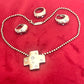 Vintage Yves Saint Laurent solid silver jewelry set displayed on red fabric: silver earrings, cross pendant necklace on beaded chain, ring,