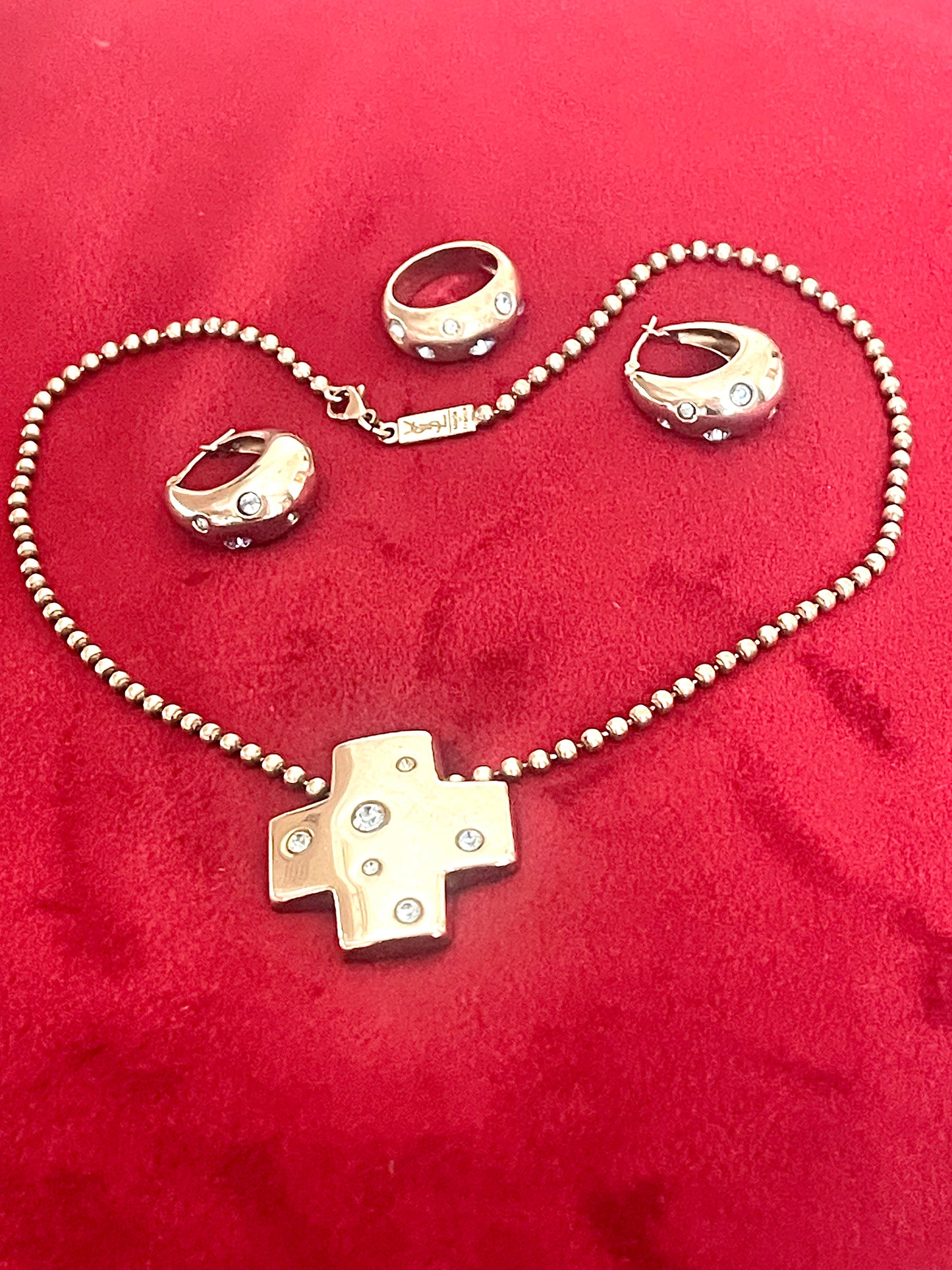 Vintage Yves Saint Laurent solid silver jewelry set displayed on red fabric: silver earrings, cross pendant necklace on beaded chain, ring,