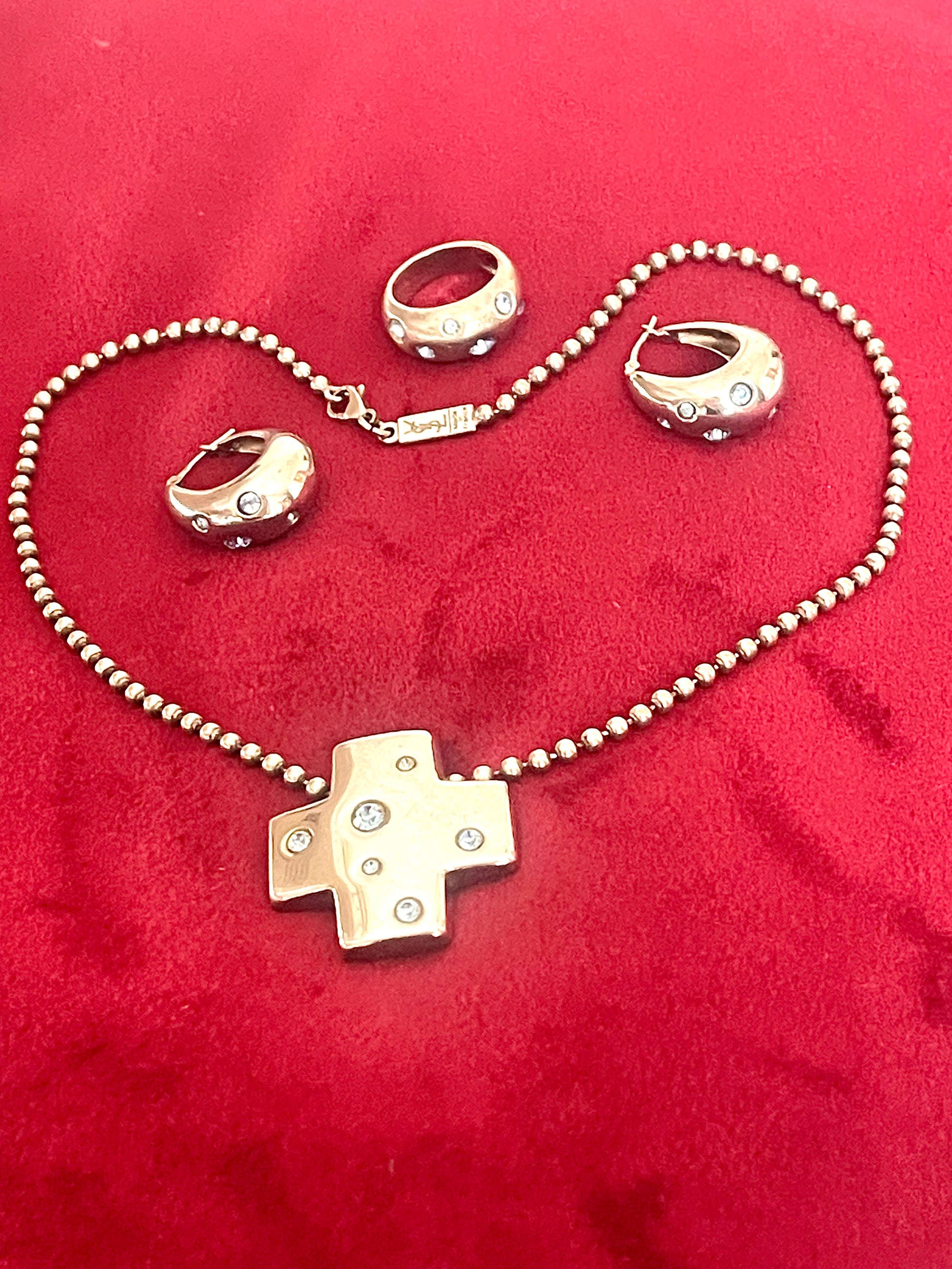 Vintage Yves Saint Laurent solid silver jewelry set displayed on red fabric: silver earrings, cross pendant necklace on beaded chain, ring,