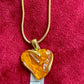 YSL Heart-shaped orange resin pendant on a gold chain with a ruler for scale on a red background
