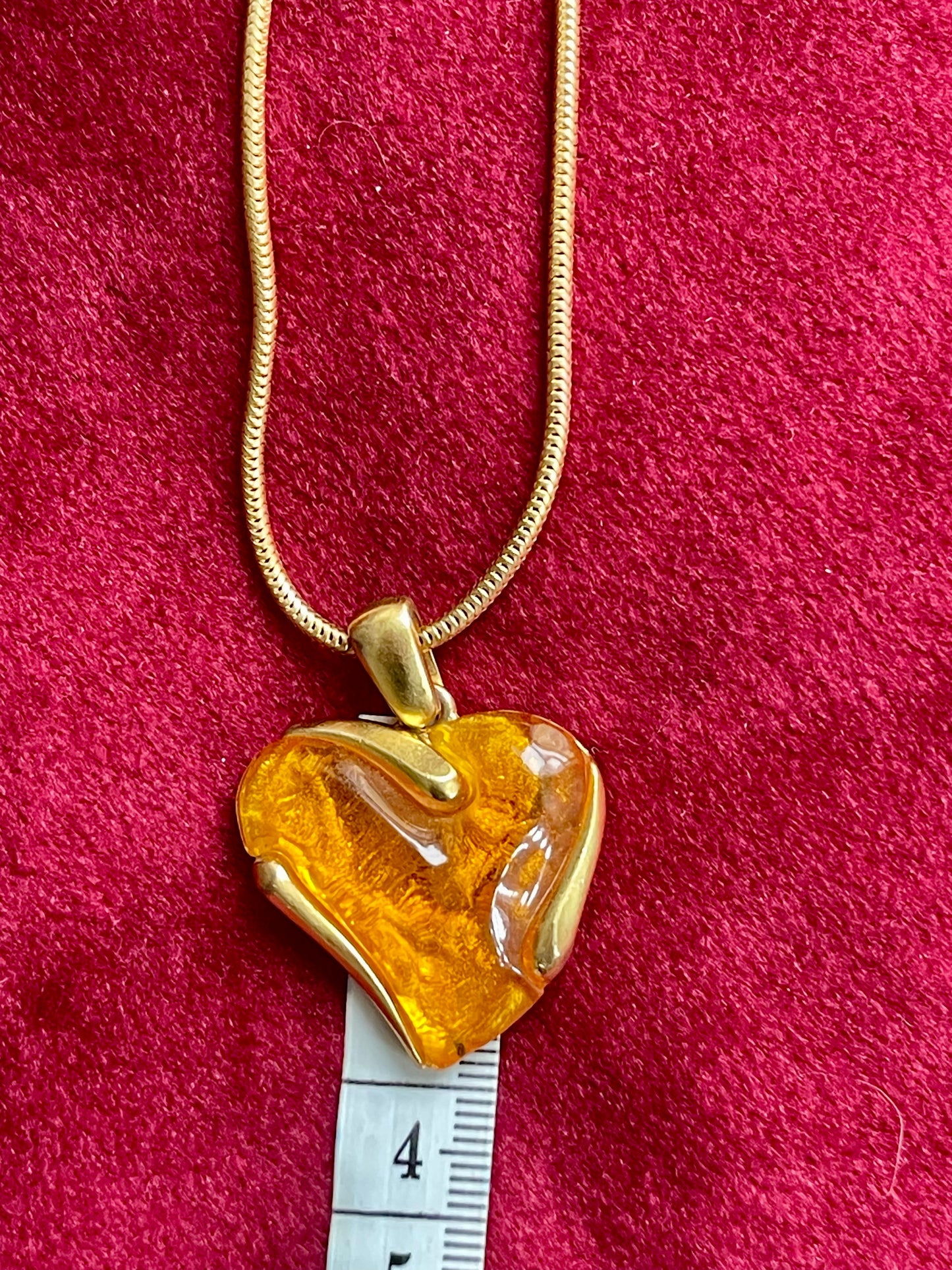 YSL Heart-shaped orange resin pendant on a gold chain with a ruler for scale on a red background