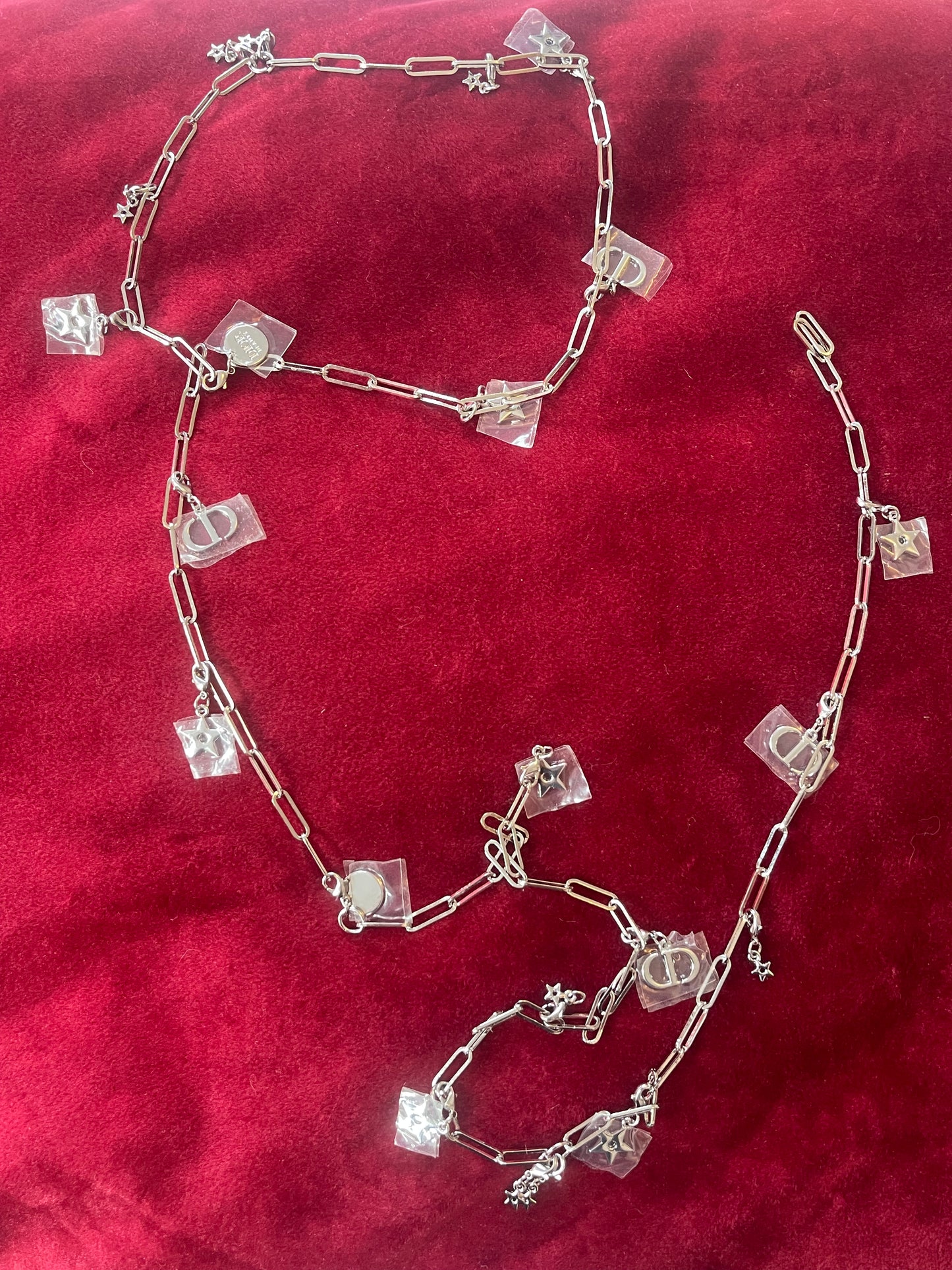 Two connected upcycled Dior Beauté phone charm necklace with removable silver-tone charms on a red background 