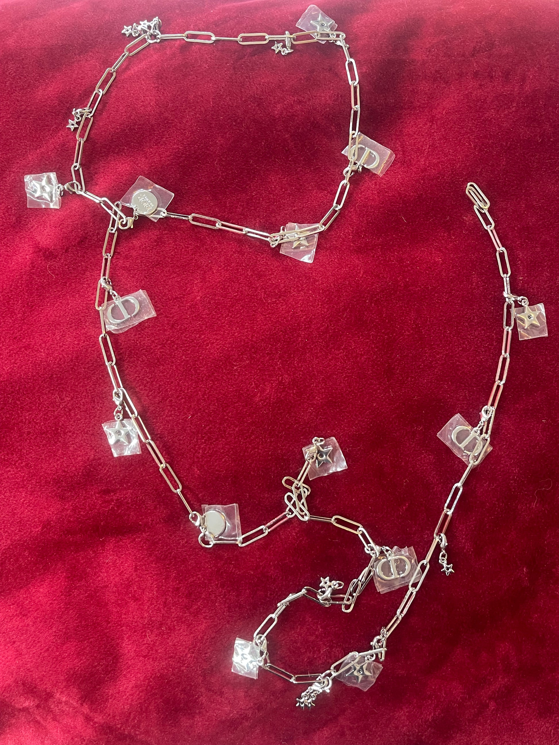 Two connected upcycled Dior Beauté phone charm necklace with removable silver-tone charms on a red background 