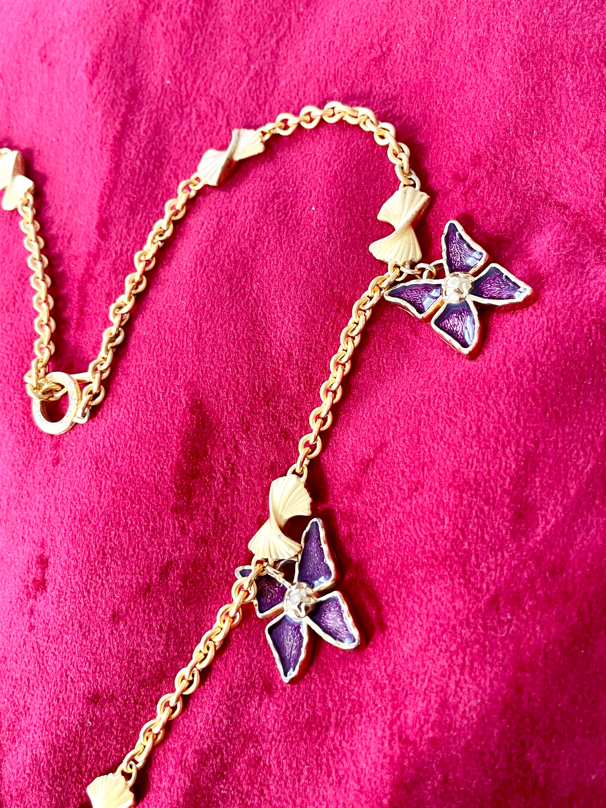 Side view of Vintage 80s five Yves Saint Laurent Butterfly Enameled pendants mounted on a Nina Ricci gold necklace, displayed on a red velvet background 