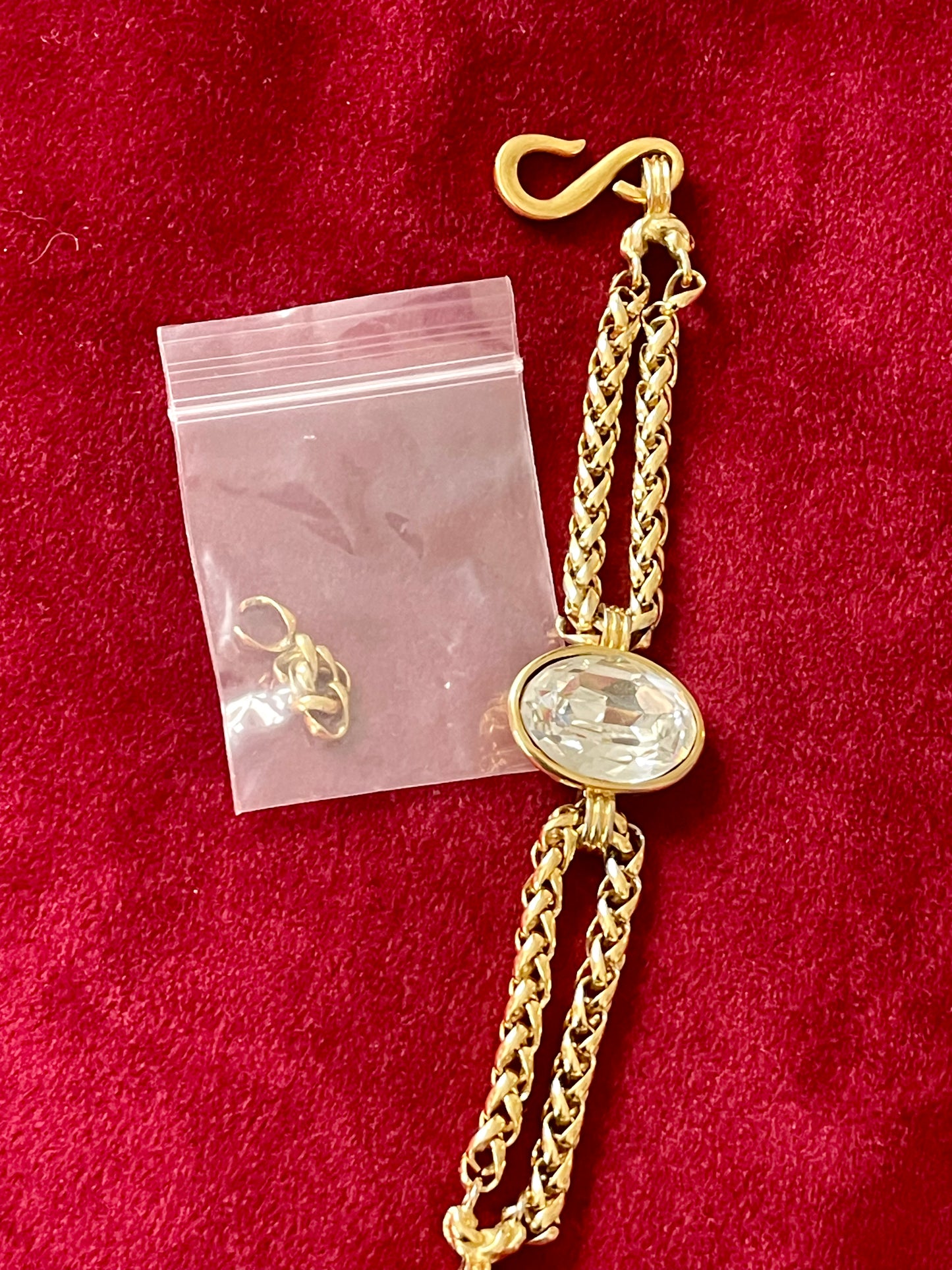 YSL gold tone statement bracelet with oval crystal centerpiece And removed hoops for smaller size on a red background 