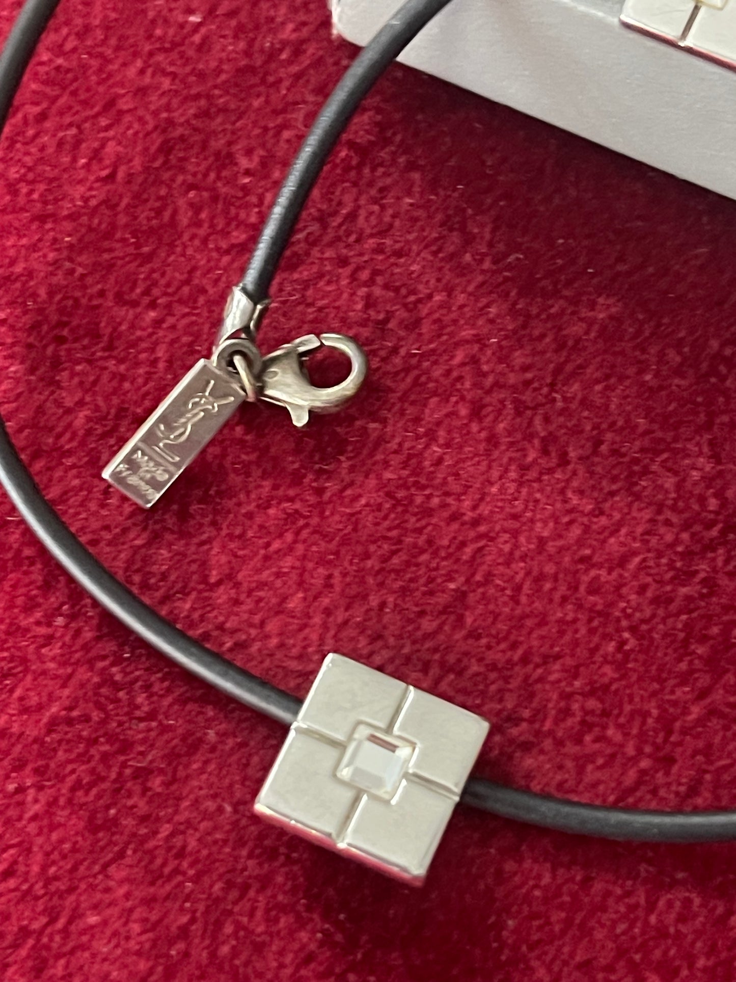 Detailed view of vintage YSL silver 925 pendant on a black cord photographed on red velvet.