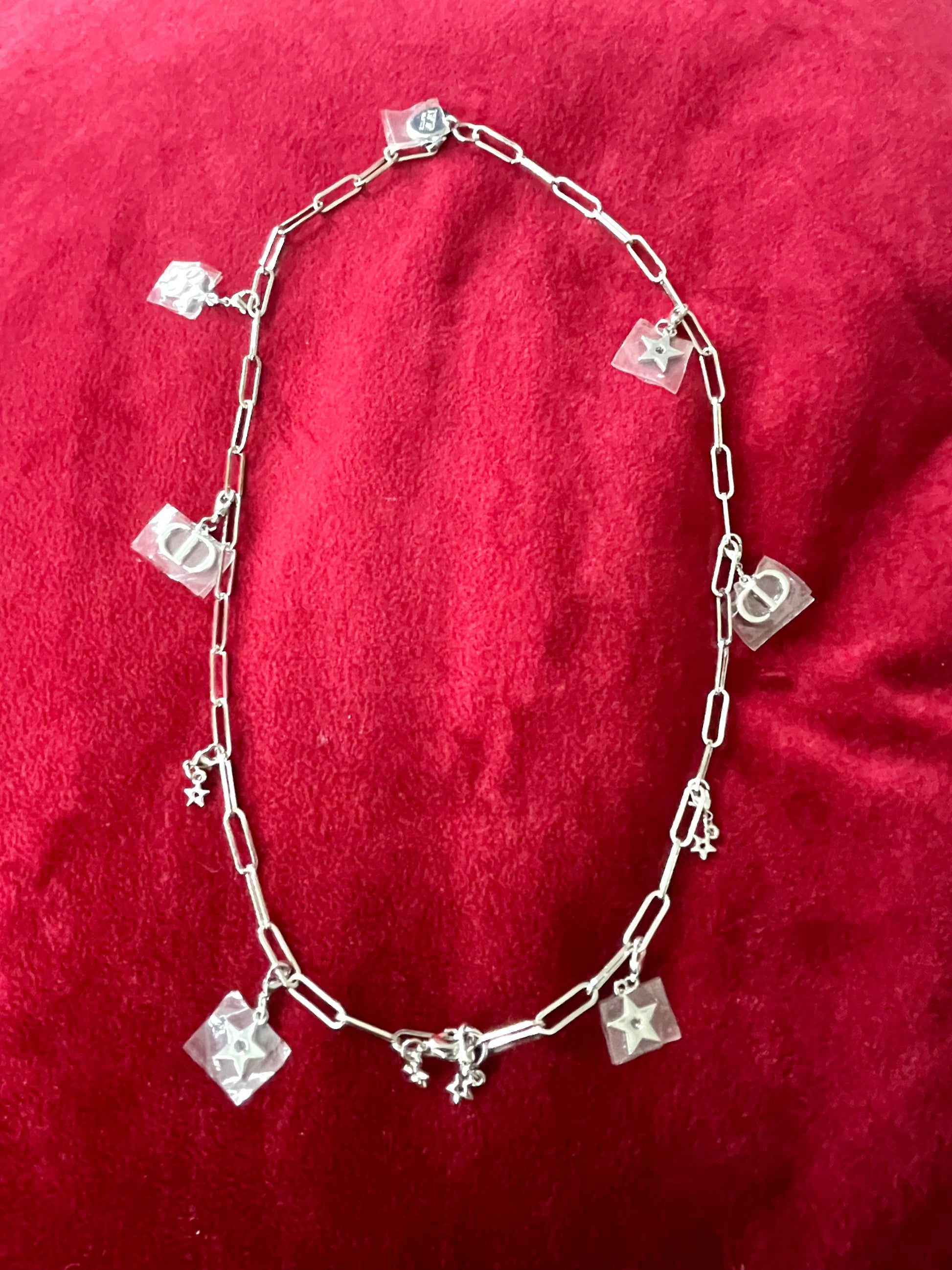 Upcycled Dior Beauté phone charm necklace with removable silver-tone charms On a red background 