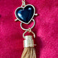 Close-up of black resin heart pendant paired with Yves Saint Laurent gold chain tassel charm on a red velvet background