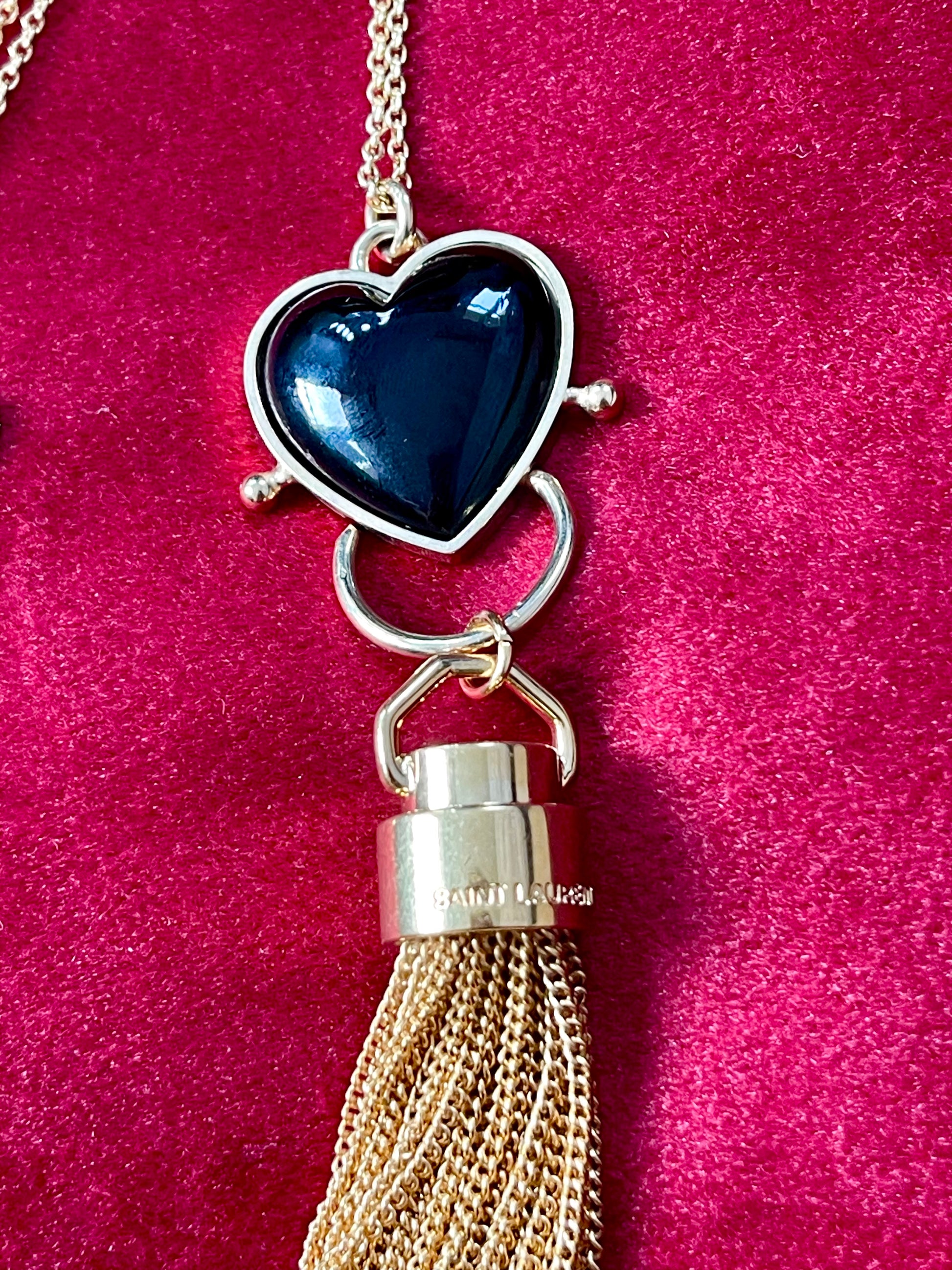 Close-up of black resin heart pendant paired with Yves Saint Laurent gold chain tassel charm on a red velvet background