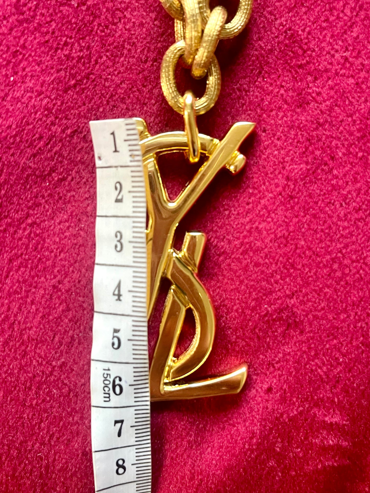 Close-up of oversized gold-plated Yves Saint Laurent logo pendant with measuring tape showing size