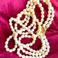 Close-up of gold-tone sculptural clasp with domed faux pearl on a vintage YSL pearl necklace, held in hand to show detail and hallmark