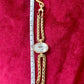 YSL gold tone statement bracelet with oval crystal centerpiece And a measuring tape on a red background 