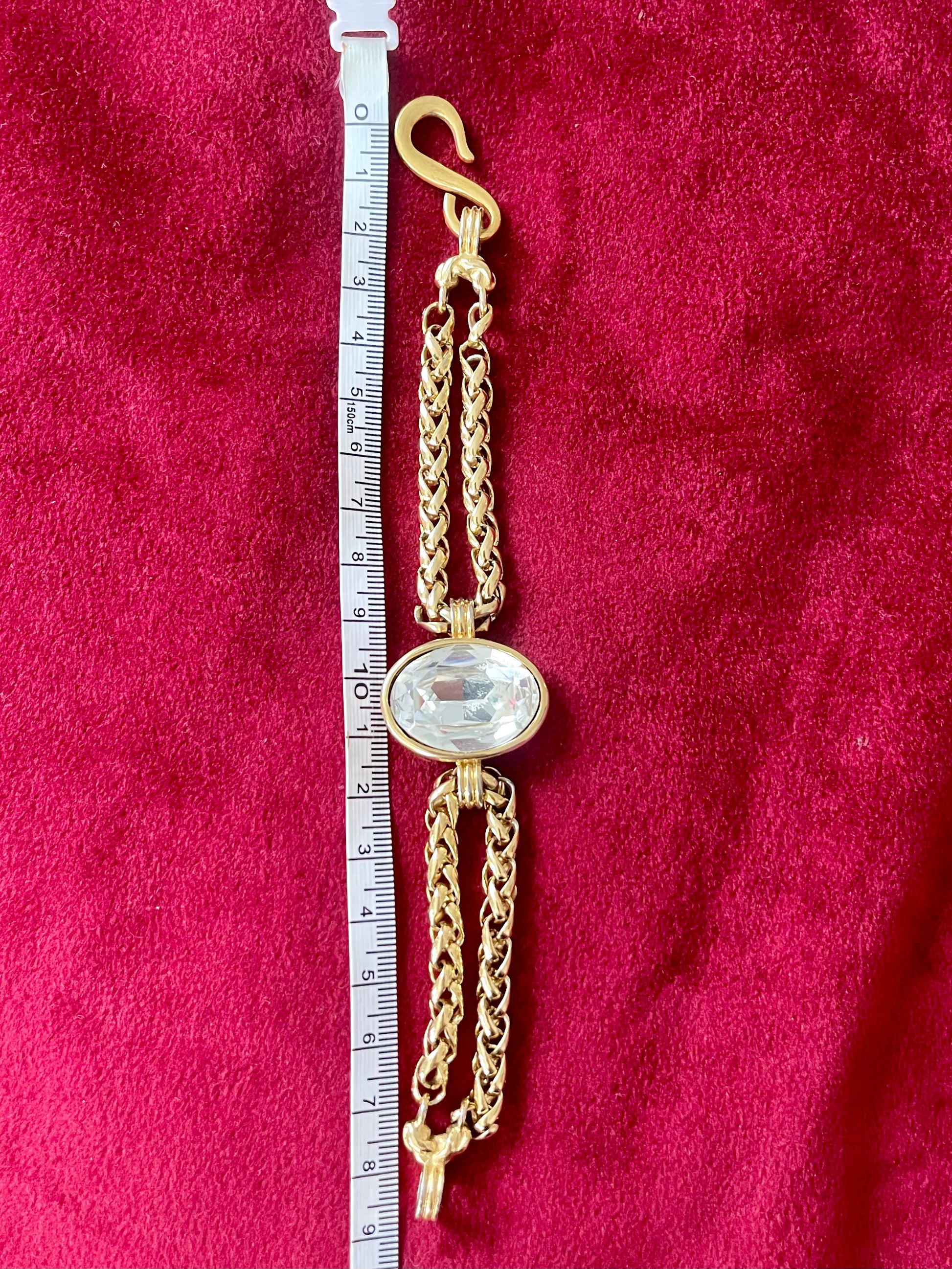 YSL gold tone statement bracelet with oval crystal centerpiece And a measuring tape on a red background 