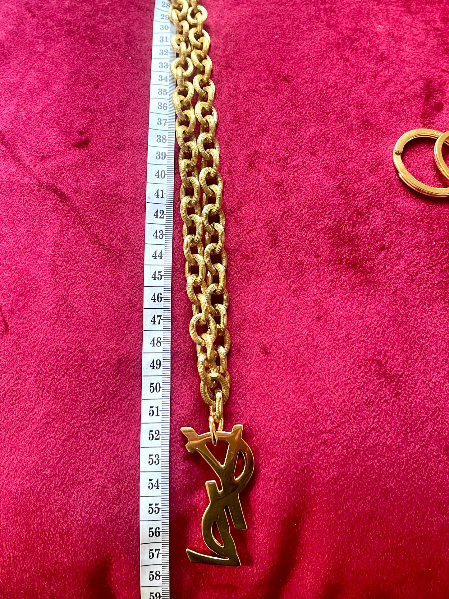 Upcycled vintage Yves Saint Laurent gold-plated logo pendant on long stainless steel chain necklace, shown with measuring tape for scale