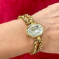 YSL gold tone statement bracelet with oval crystal centerpiece Worn wrist with a red background 