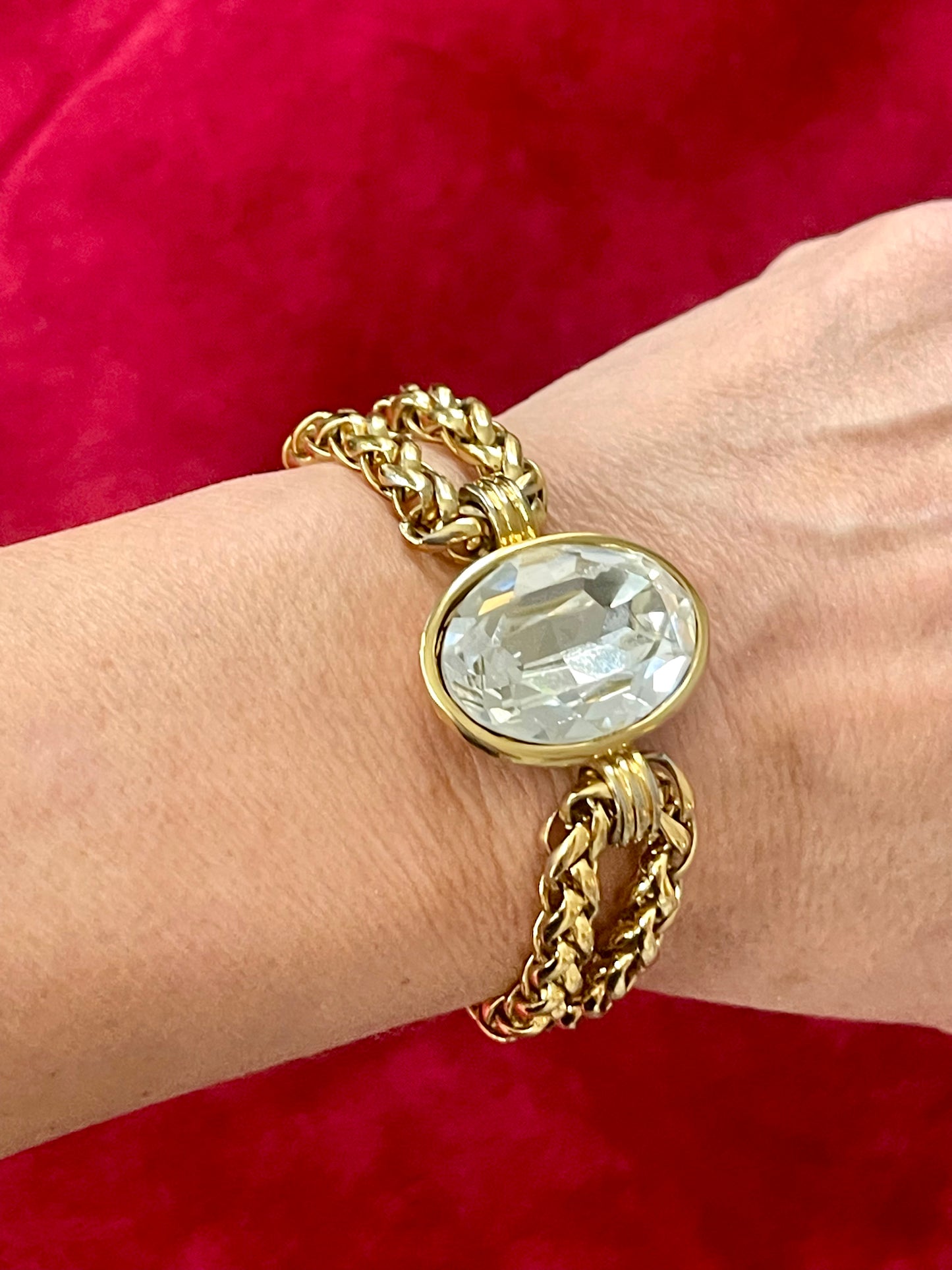 YSL gold tone statement bracelet with oval crystal centerpiece Worn wrist with a red background 