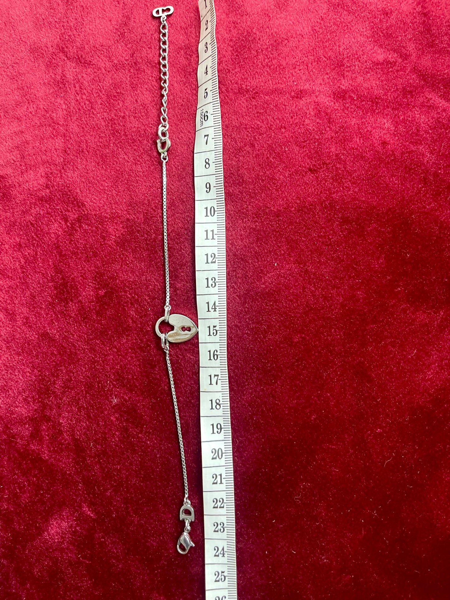 Silver Dior bracelet heart lock pendant with a clasp on a red textured background with a measuring tape.