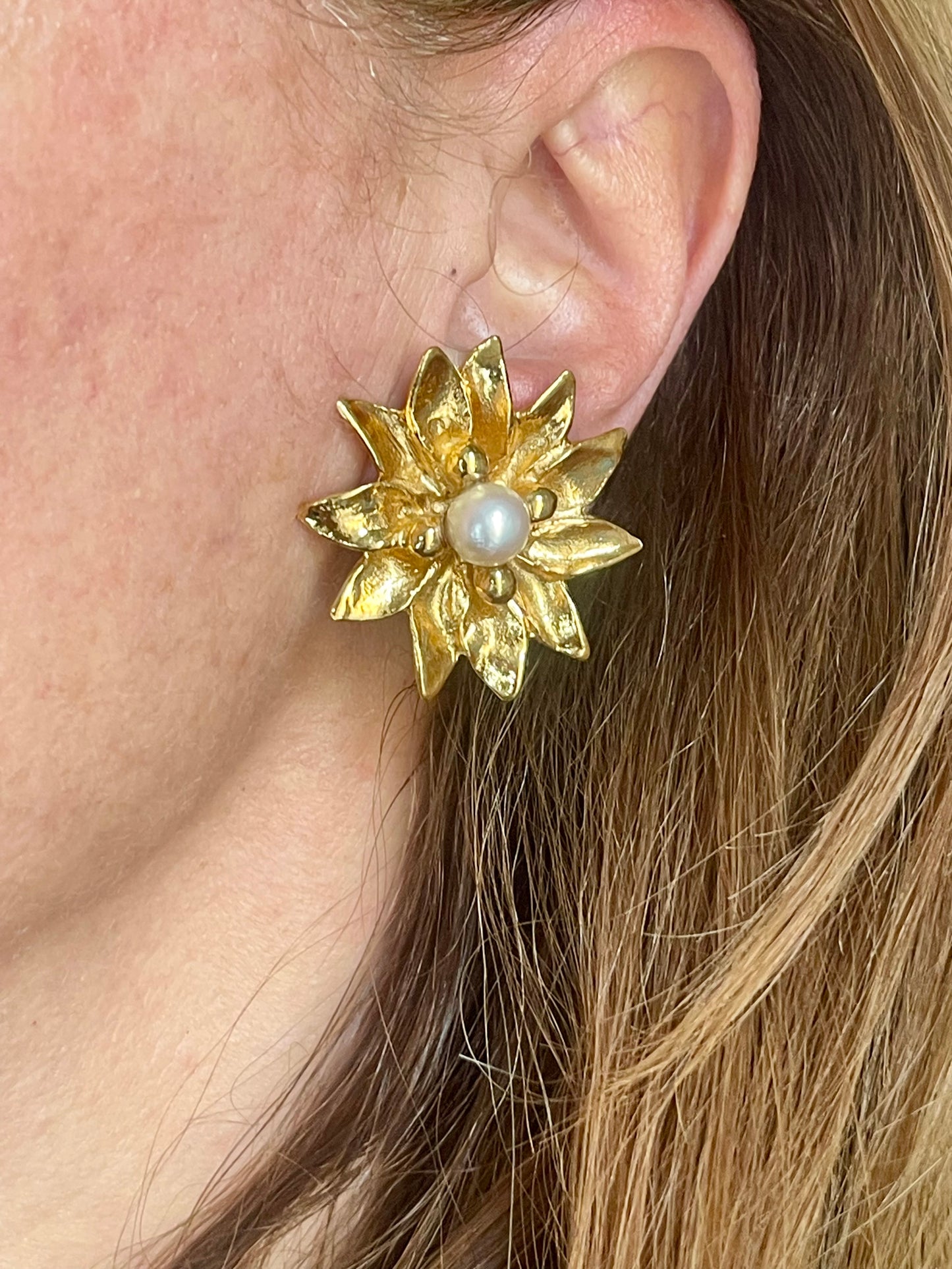 Yves Saint Laurent Gold flower-shaped earring with a pearl center worn by a person.