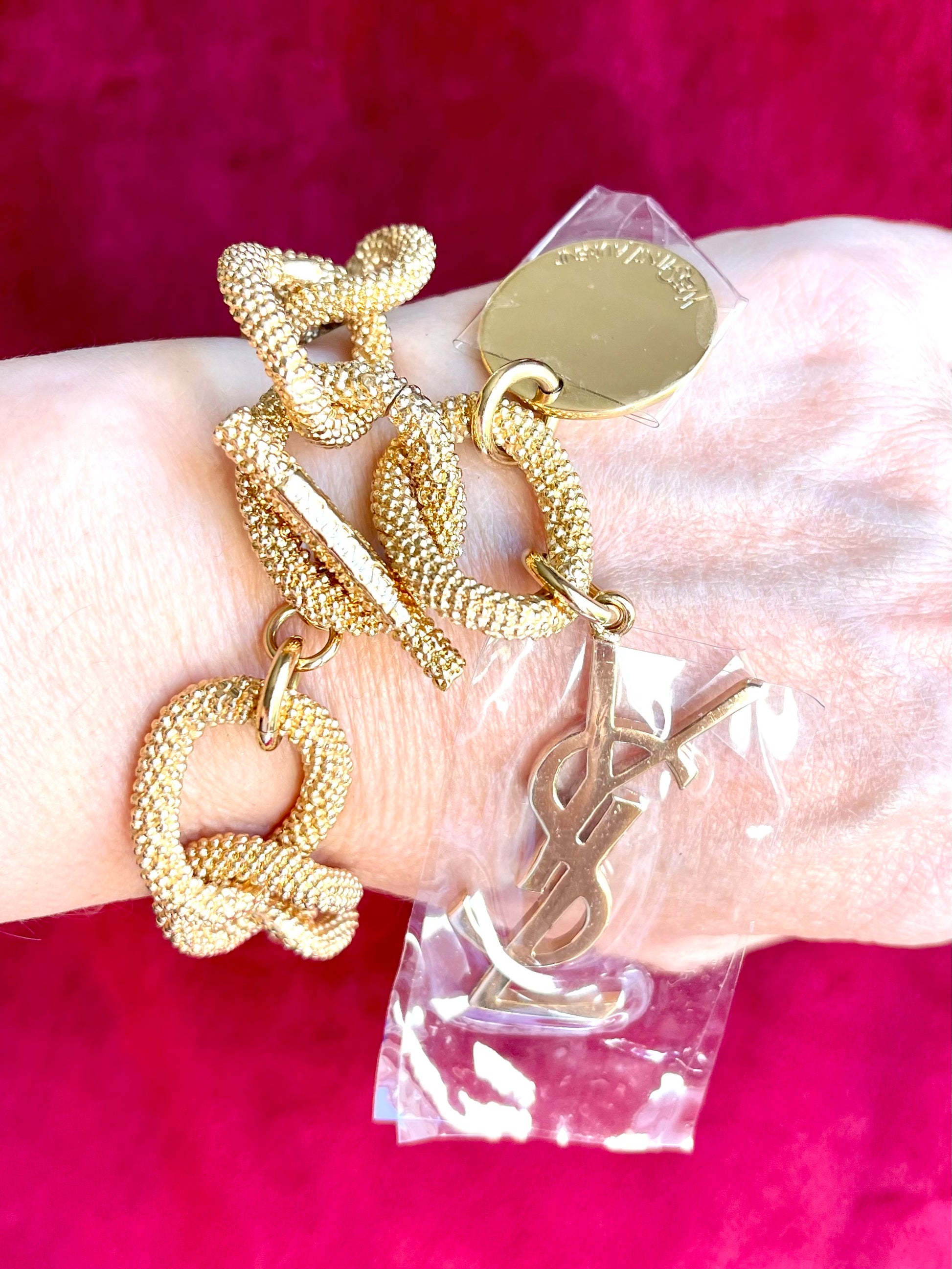 Gold-tone vintage Yves Saint Laurent chain bracelet worn on wrist with YSL logo charm and medallion on red background 