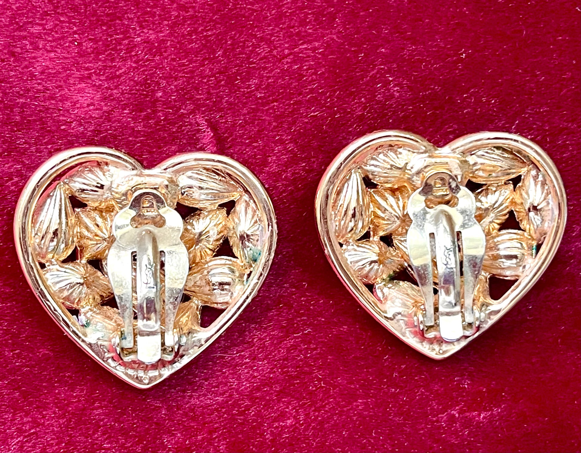 Back view showing signature of a Pair of 3 cm gold-tone vintage Yves Saint Laurent heart-shaped clip-on earrings decorated with multi-coloured crystals, displayed on a red background