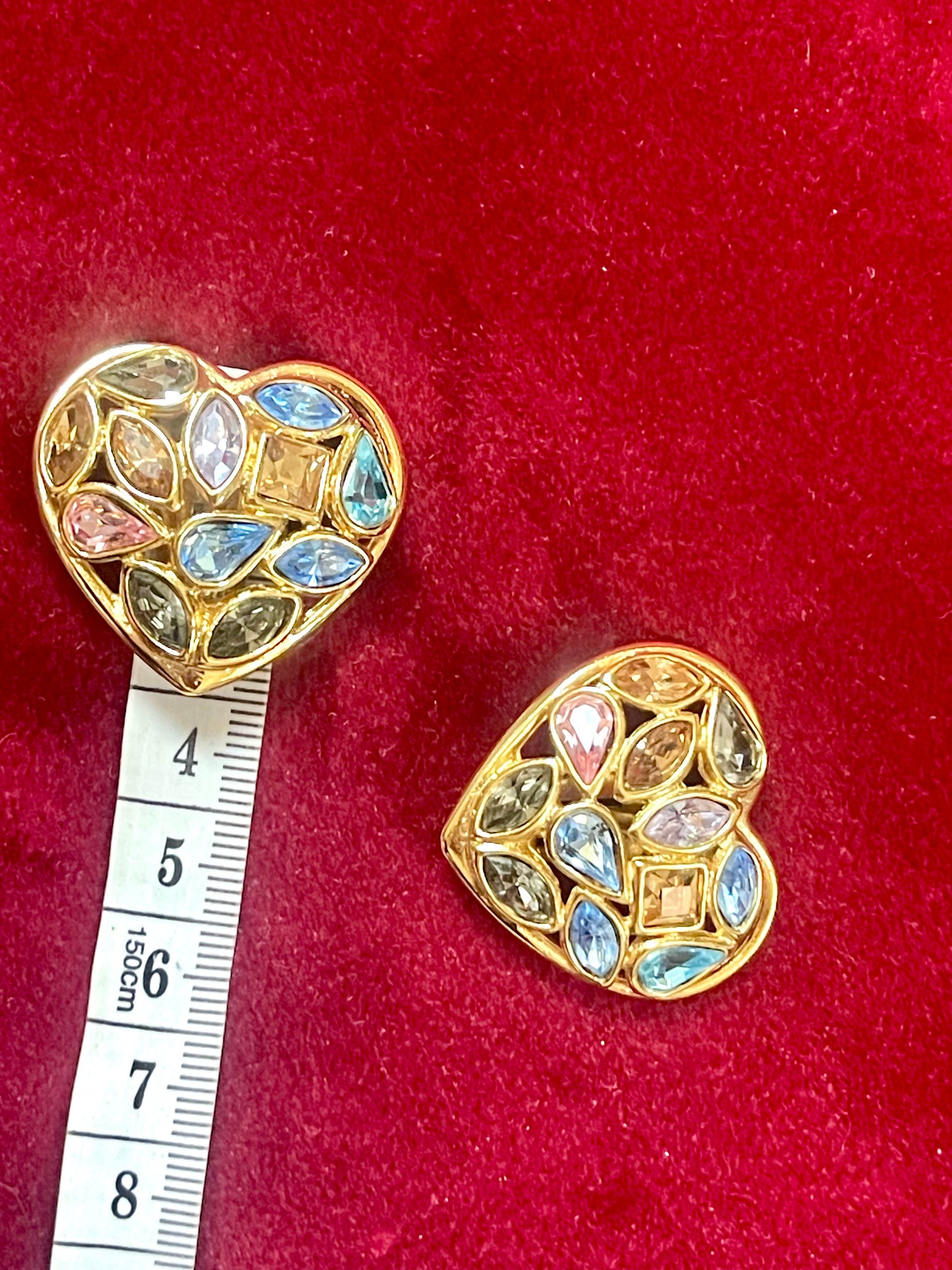 Pair of 3 cm gold-tone vintage Yves Saint Laurent heart-shaped clip-on earrings decorated with multi-coloured crystals, displayed on a red background Using a Measuring Tape 