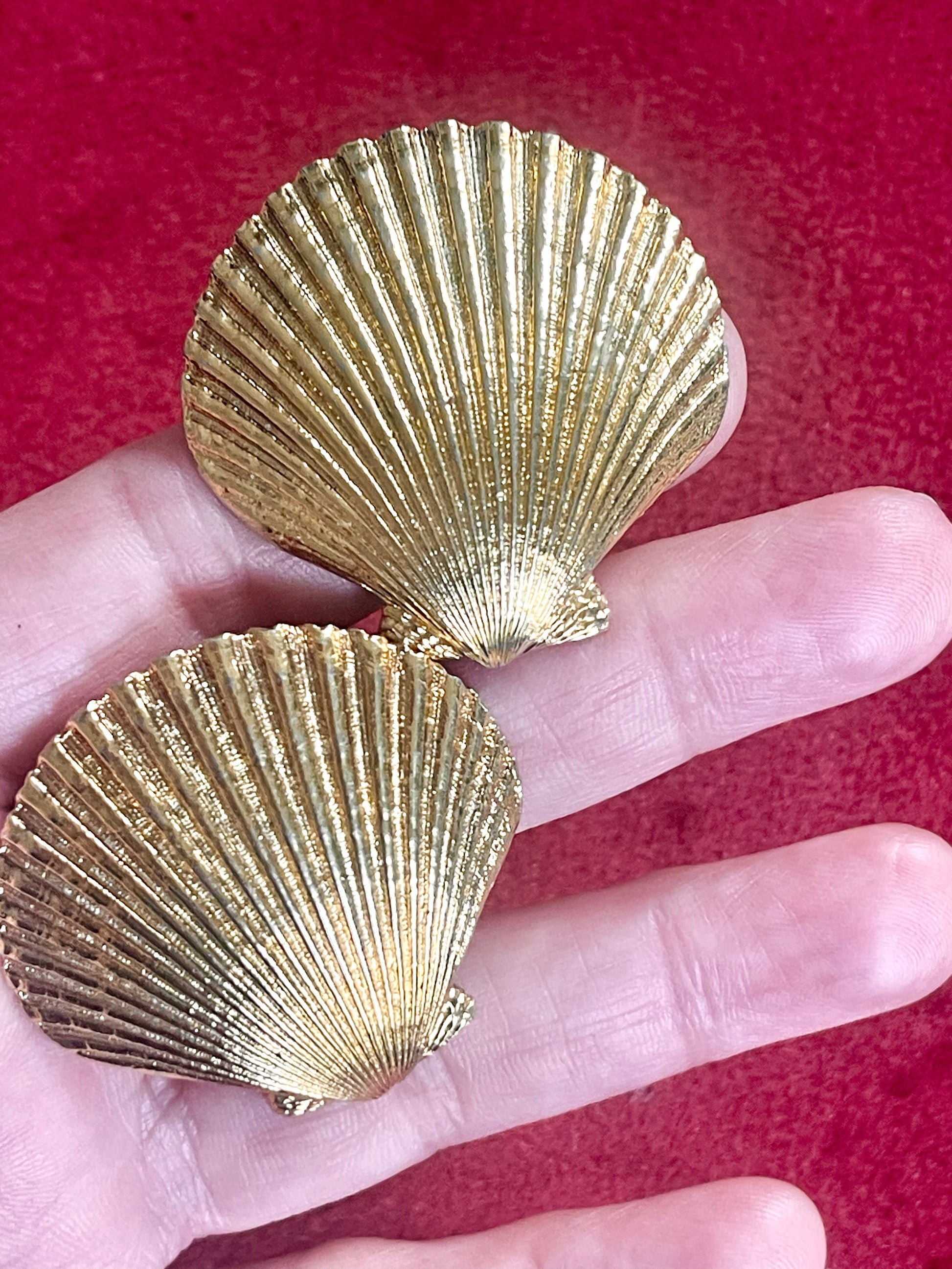 Gold-tone 80s vintage Yves Saint Laurent shell-shaped earrings displayed on hand and a red fabric showing detailed ribbed texture
